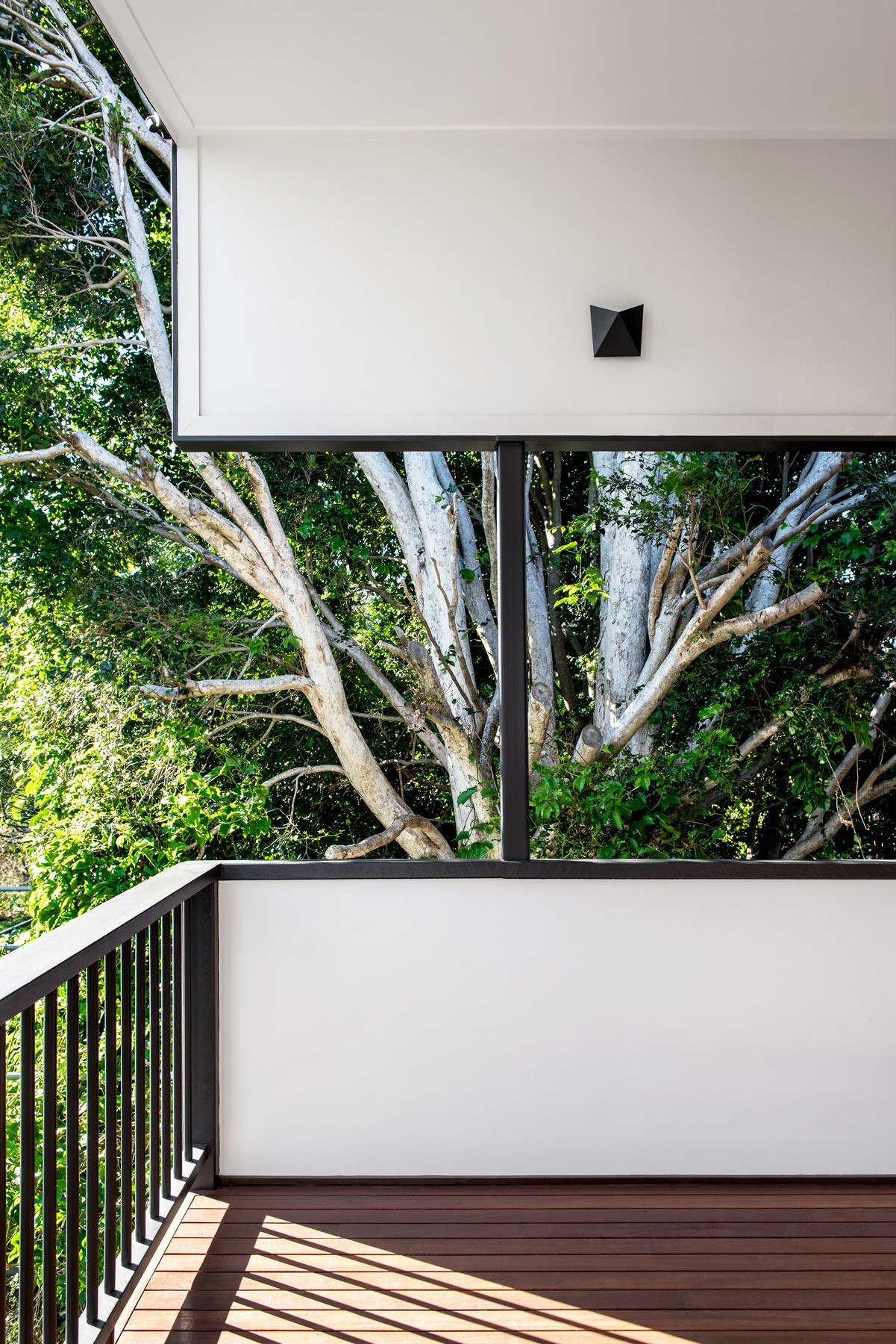 Balcony detail at Oxford Cottage, where clean white forms and dark railings frame views into the surrounding greenery.