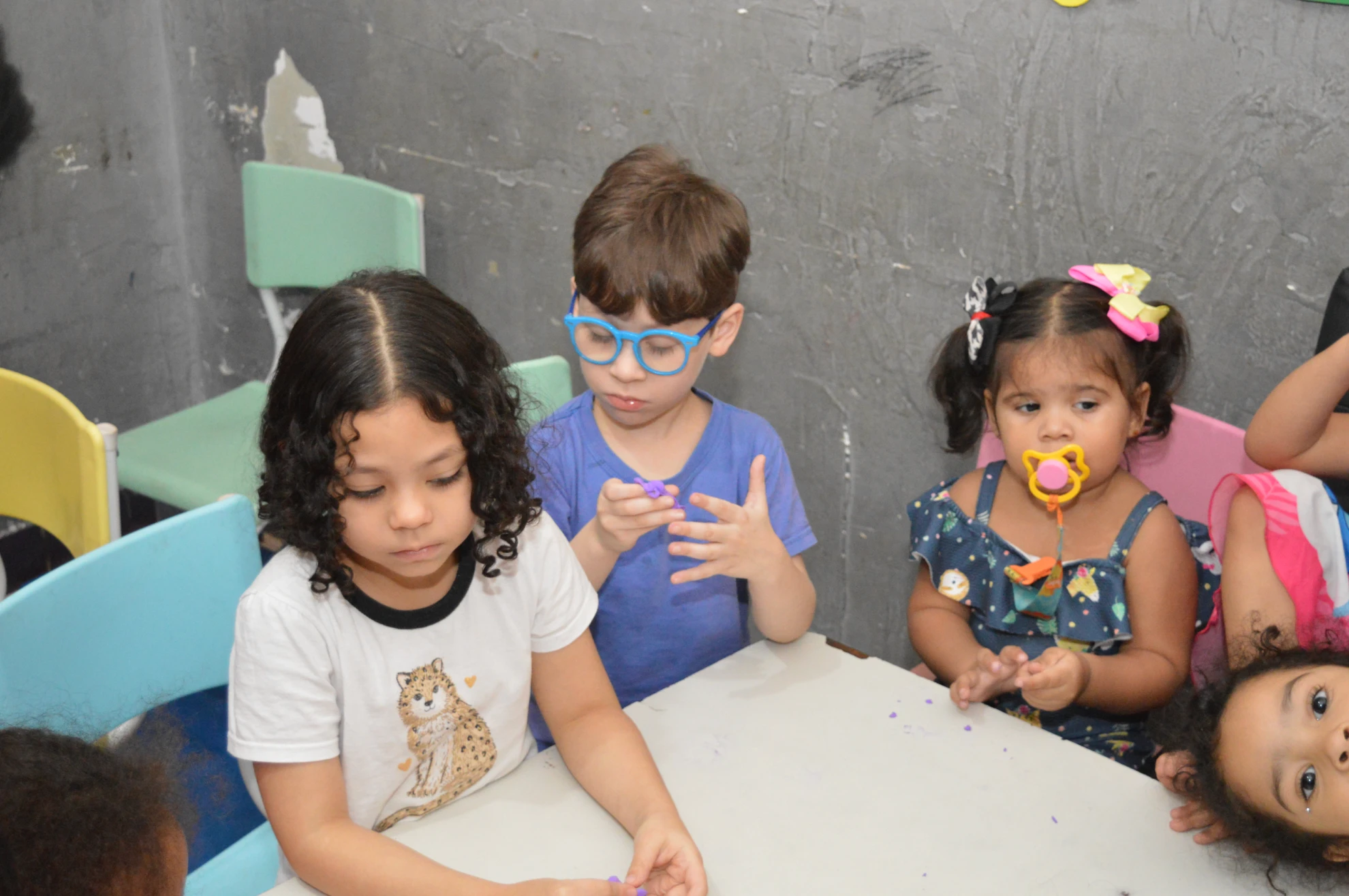 Três crianças reunidas ao redor de uma mesa, com expressão de curiosidade e concentração.