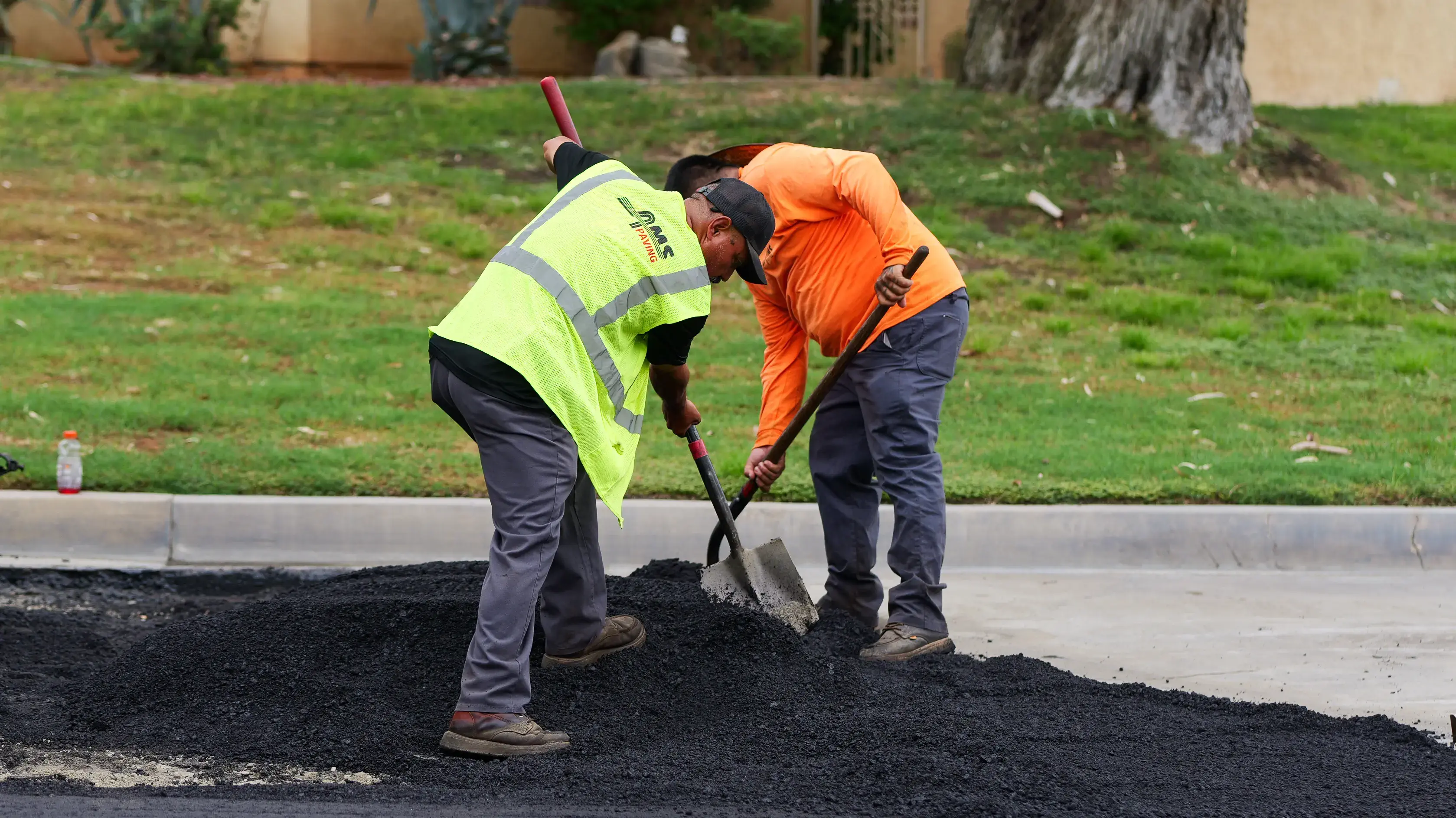 Asphalt crew rakers and shovelers moving pile of hot mix asphalt material