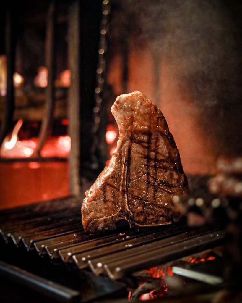 A perfectly grilled steak on a fire grill, showcasing grill marks, with glowing embers in the background.