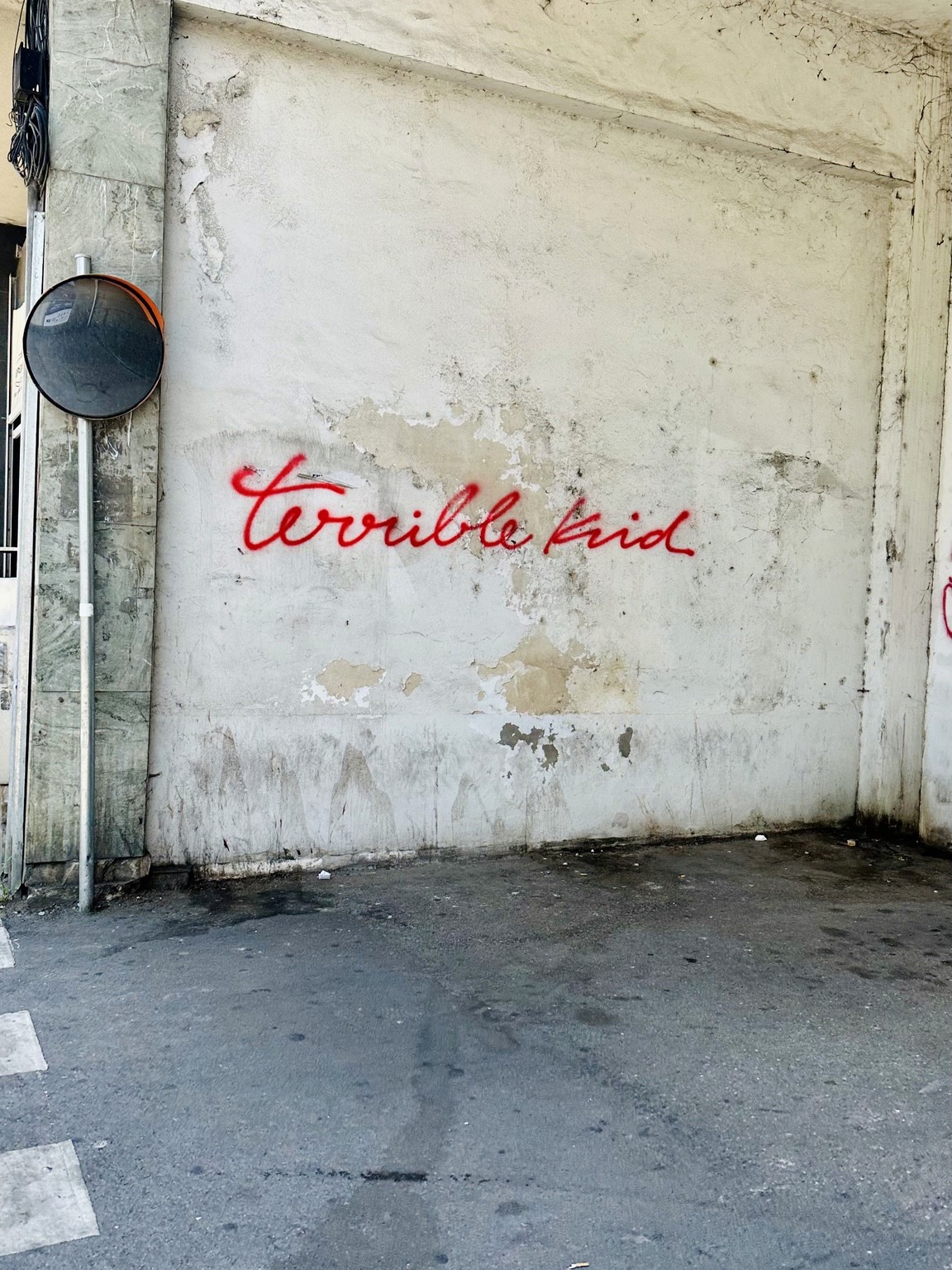 Red cursive lettering painted on a weathered pale wall beside a round mirror.