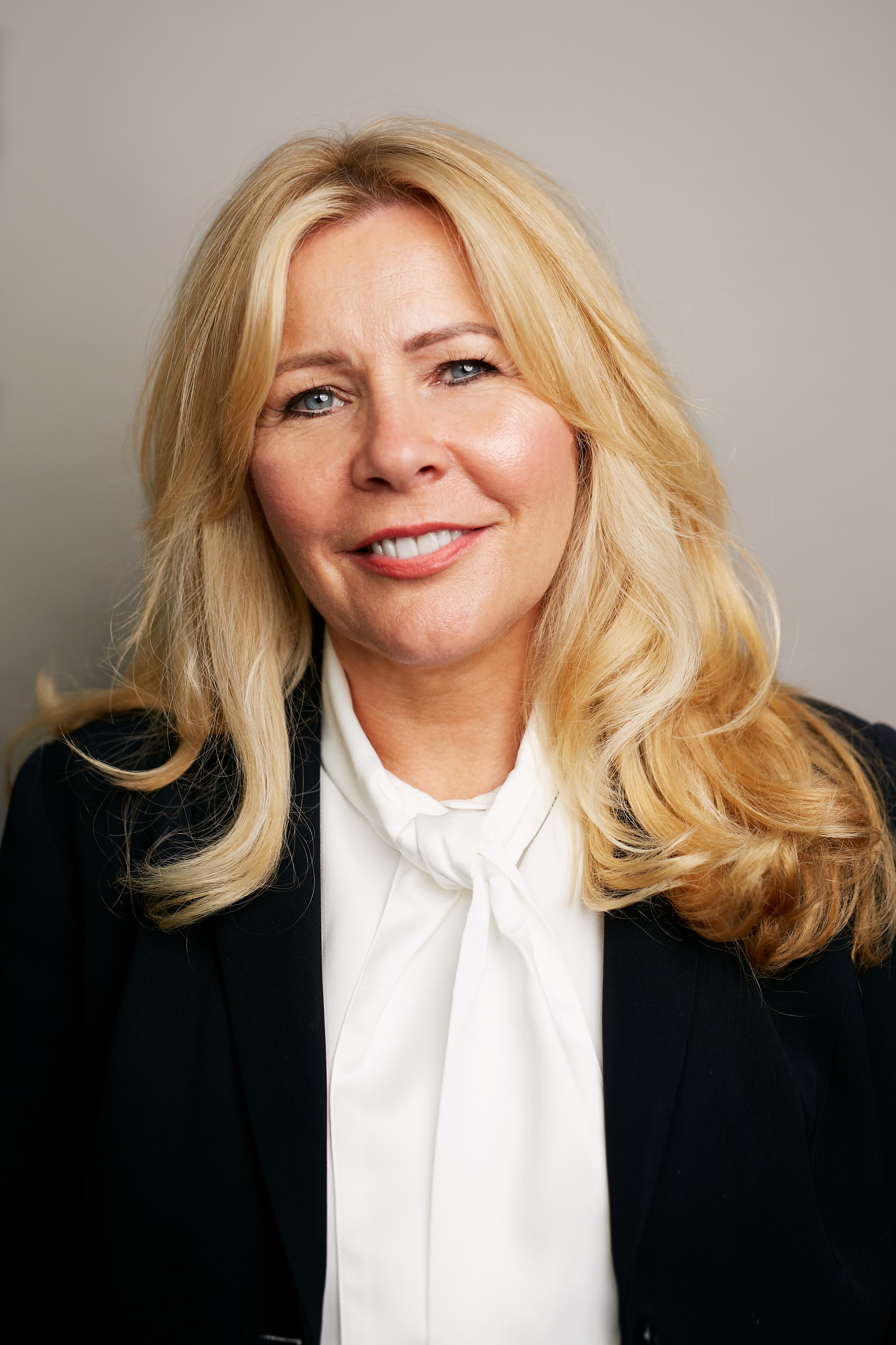 Woman with blonde hair and blue eyes smiles.