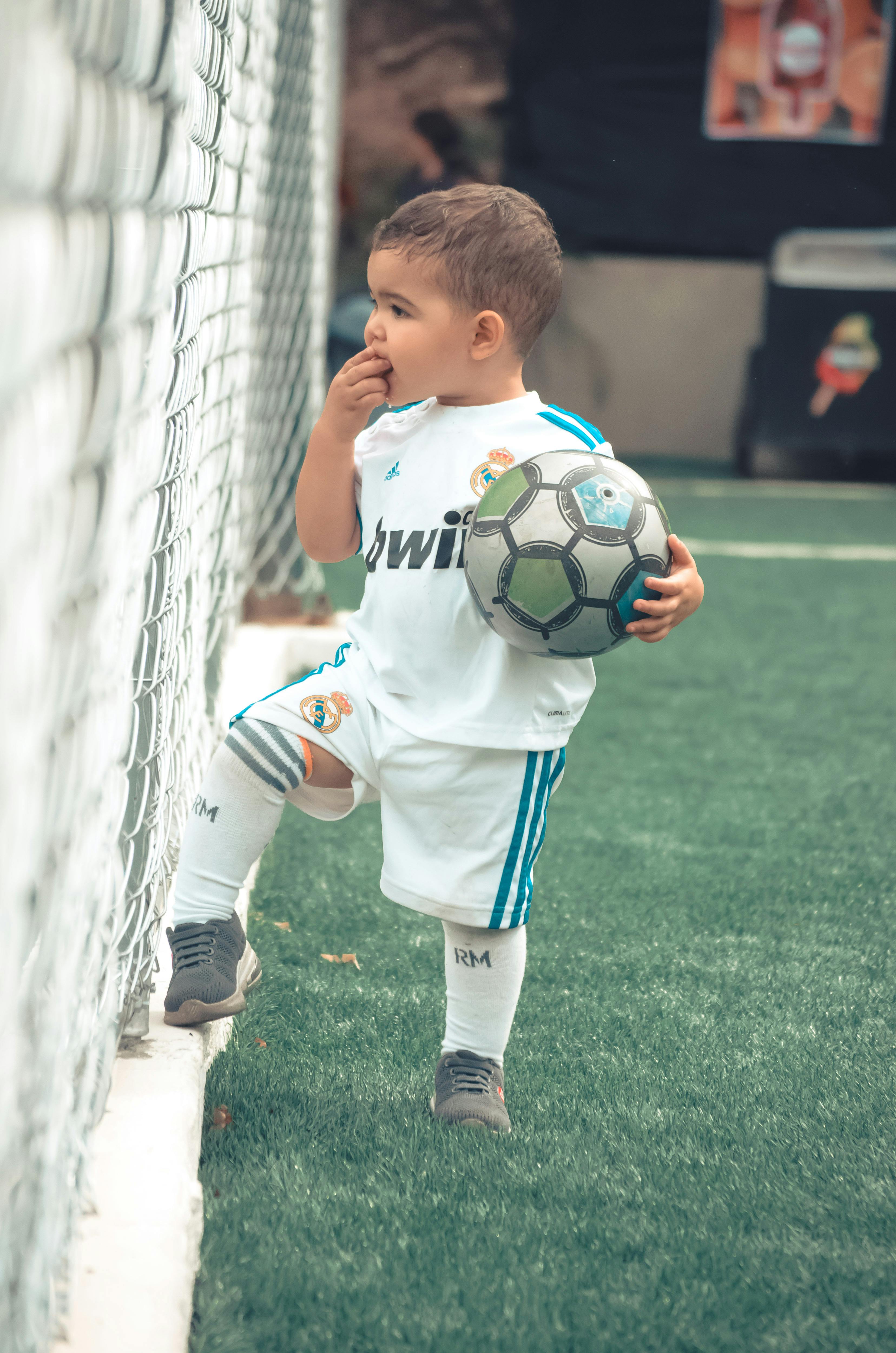 a-child-in-sportswear-holding-a-soccer-ball-on-a-football-pitch,-exhibiting-inno - norman-milwood (pexels)