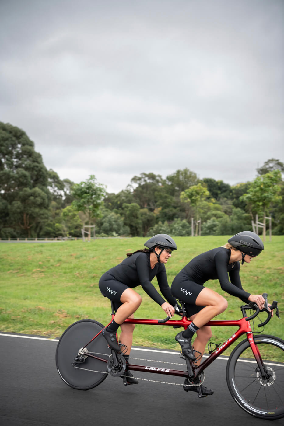 Lily and Jay cycling together in black cycling kits, around a crit track