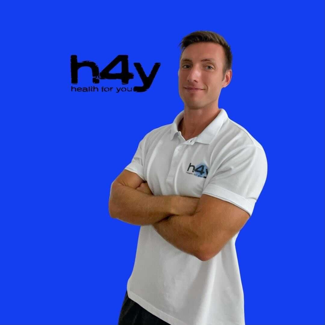 A woman with blonde bob hair in a grey coat and beige turtleneck stands against a neutral backdrop. She has a serious expression, conveying elegance.