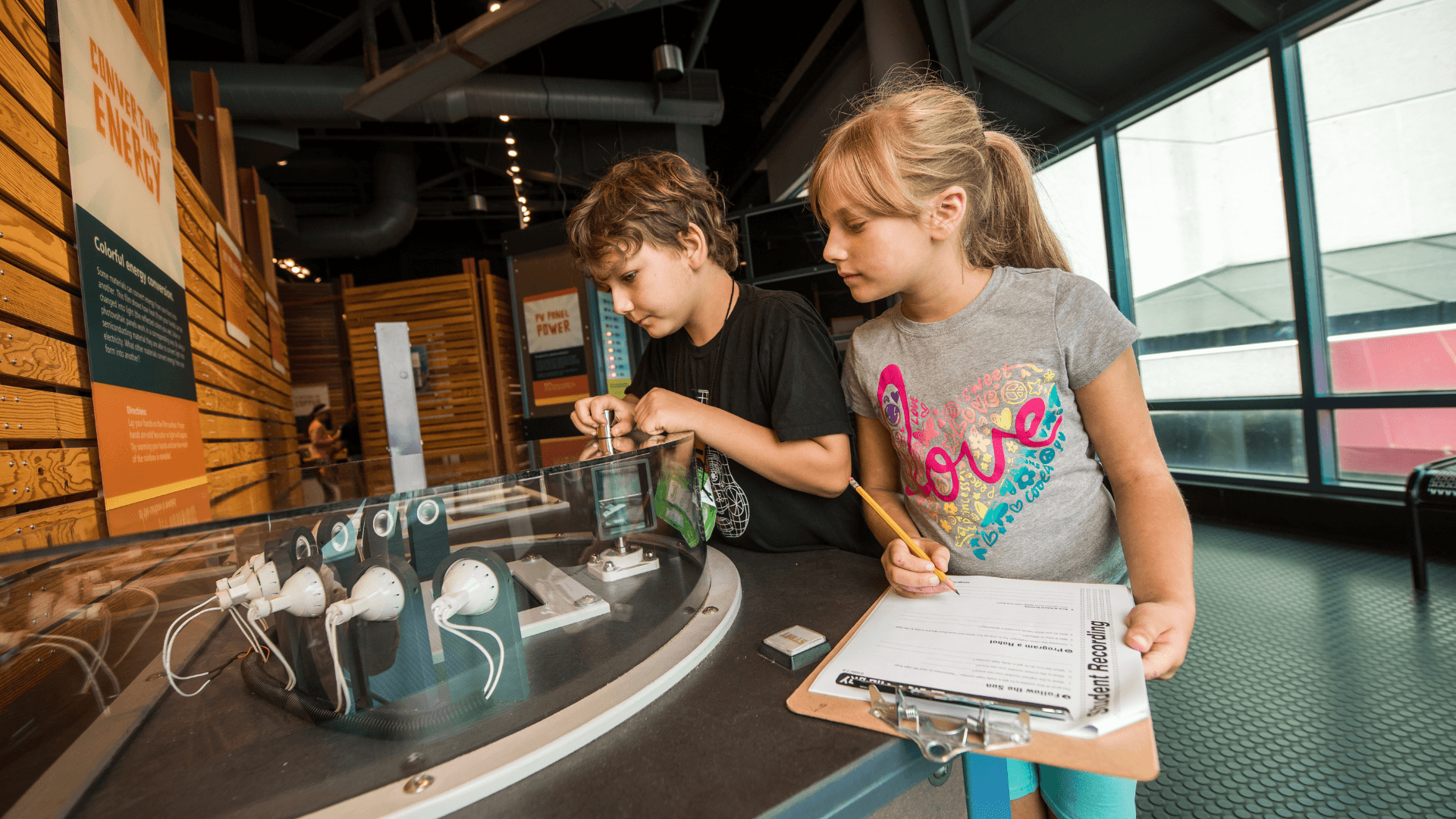 Two kids explore an exhibit while filling out a worksheet.