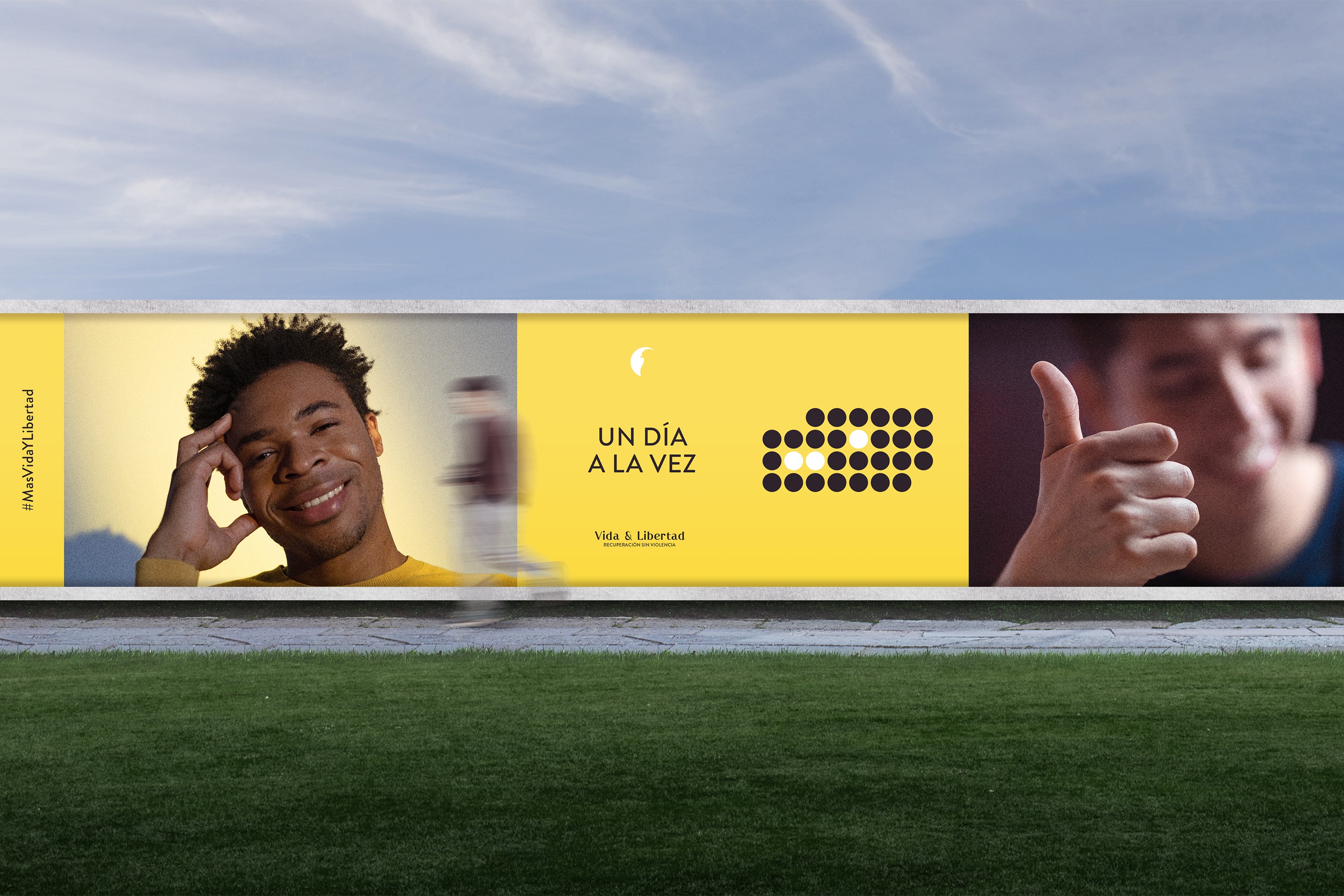Vida & Libertad outdoor banner featuring smiling portraits, bright yellow branding, and the Spanish message “Un día a la vez,” promoting hope and recovery.