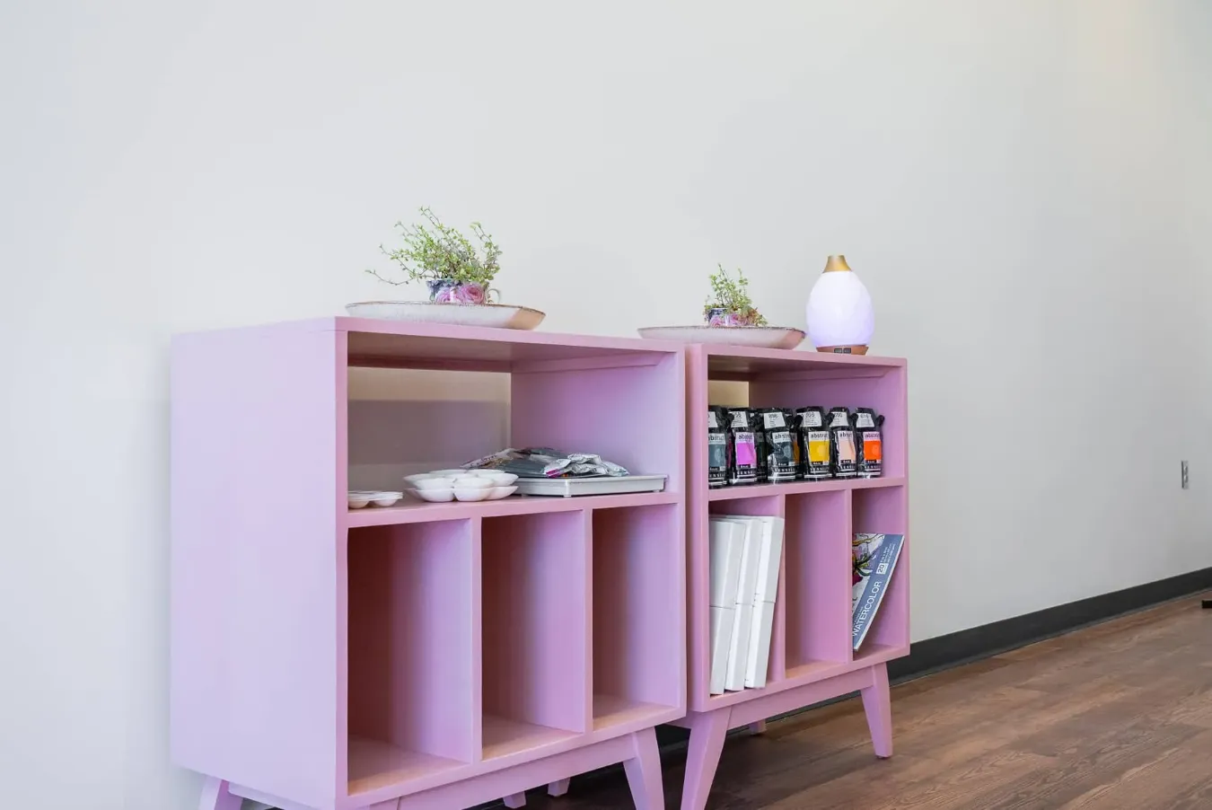 Pink studio shelving stocked with paints and art supplies.