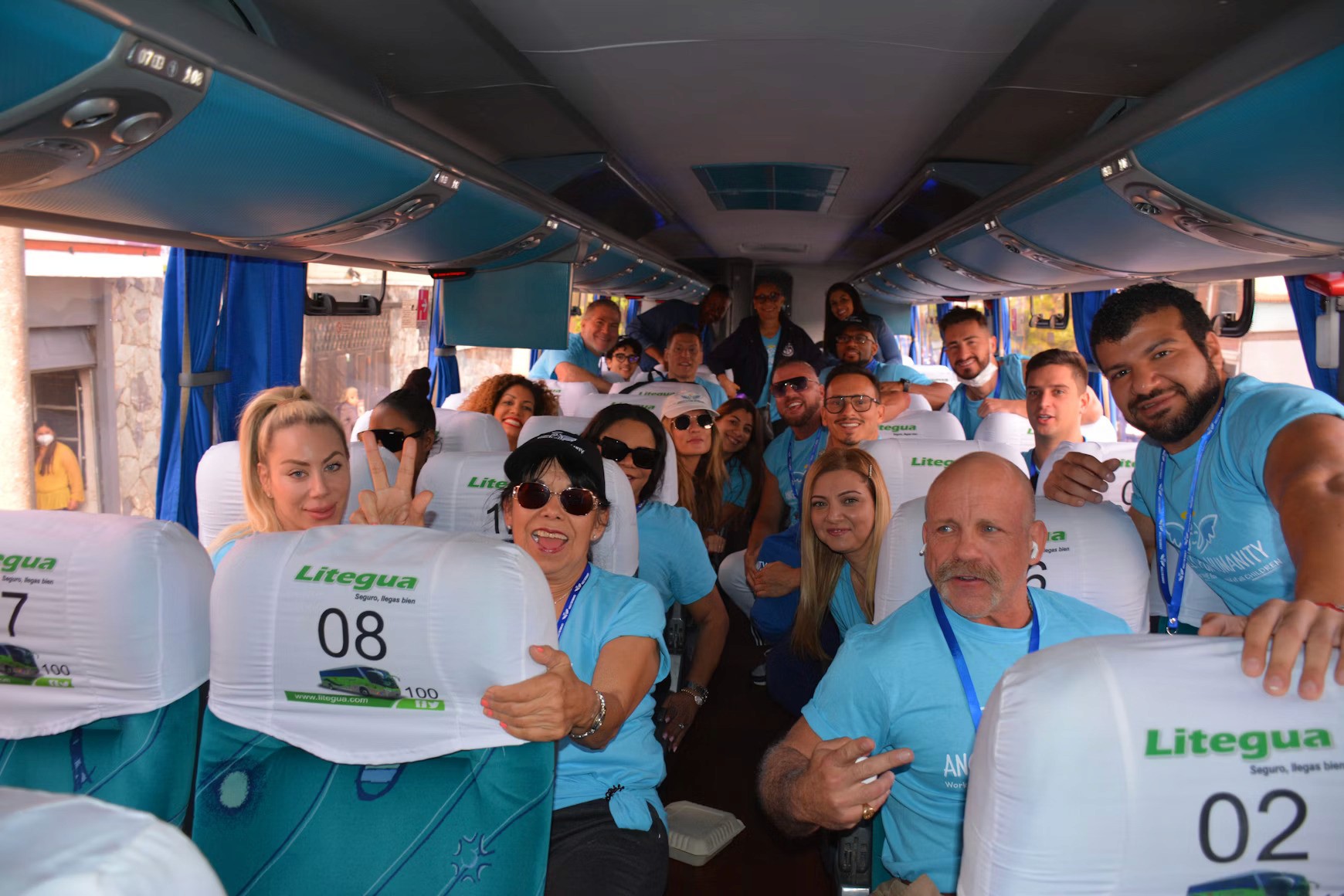 Group of people smiling inside a Litegua bus, wearing matching blue shirts, enjoying a group trip or excursion.