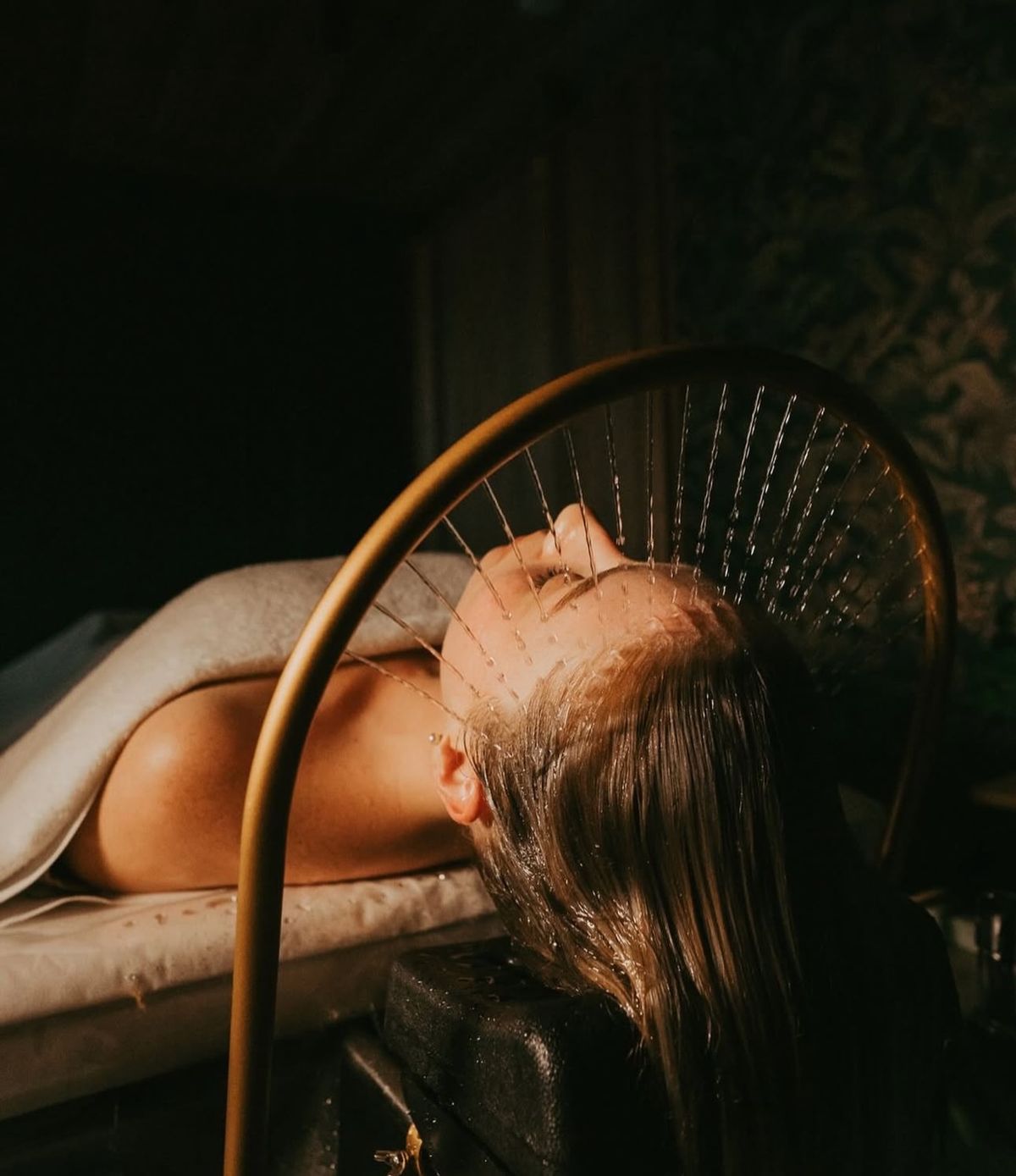 A young woman with wet hair, leaning back in a bath with her eyes closed. The sunlight reflects off the water, creating a serene and tranquil atmosphere.
