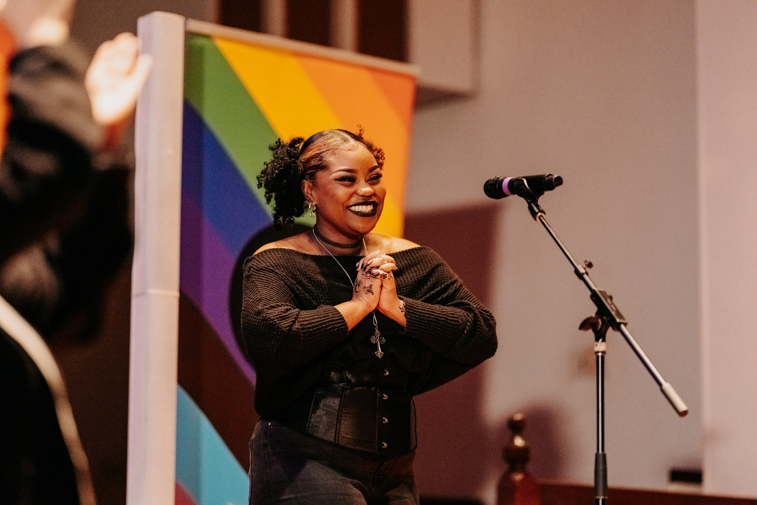 Performer smiling on stage at the Queer Open Mic (QOM) hosted by be; community in Bridgewater, Massachusetts