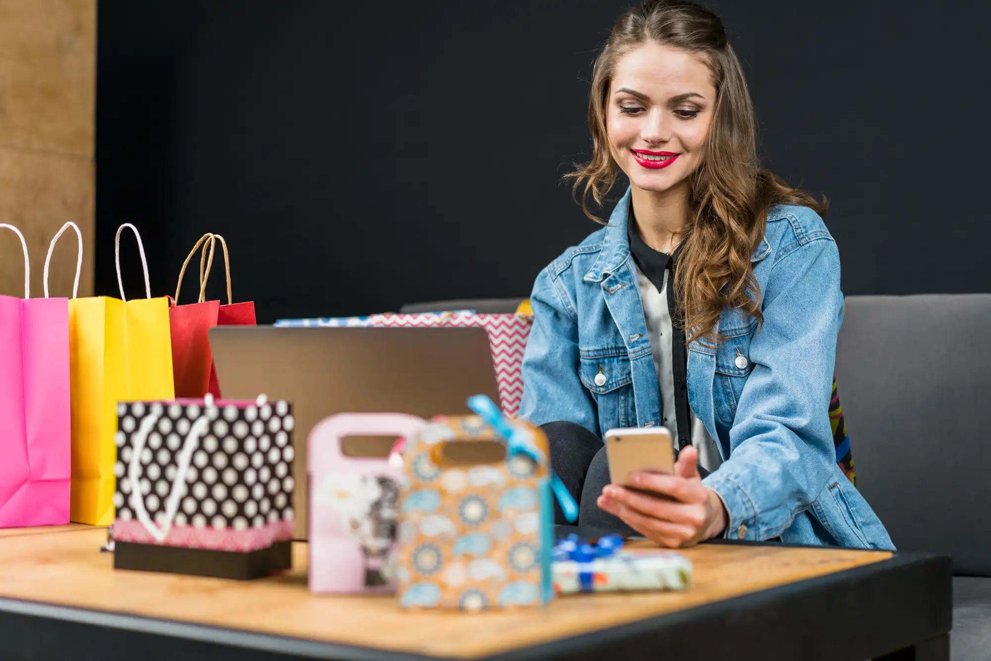 A young woman is looking at her phone, surrounded by shopping bags and boxes, highlighting the rise of mobile social commerce.