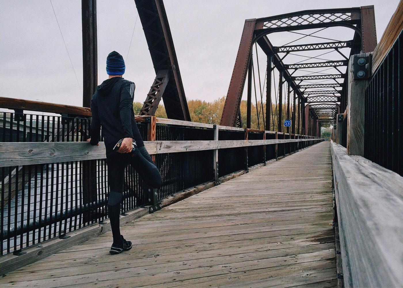 Man stretching his leg holding on to his foot on a bridge