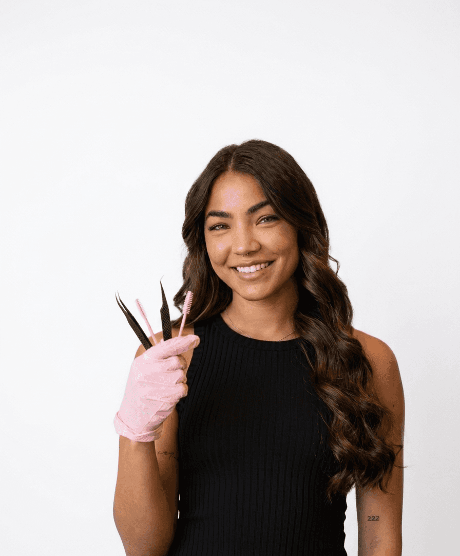 Mali Beauty owner wearing black work top, pink ppe glove whilst holidng tools used for applying eyelashes