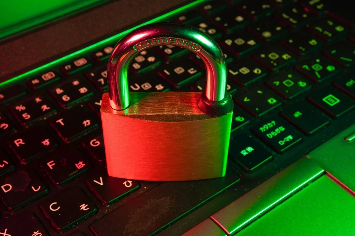 A brass padlock sits on a laptop keyboard illuminated by red and green lighting. The setup suggests a theme of digital security or data protection.