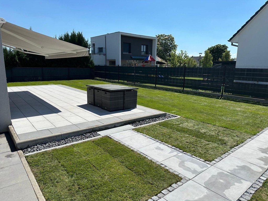 Frisch verlegter Rollrasen mit gepflasterter Terrasse und Gehweg in einem modernen Garten.