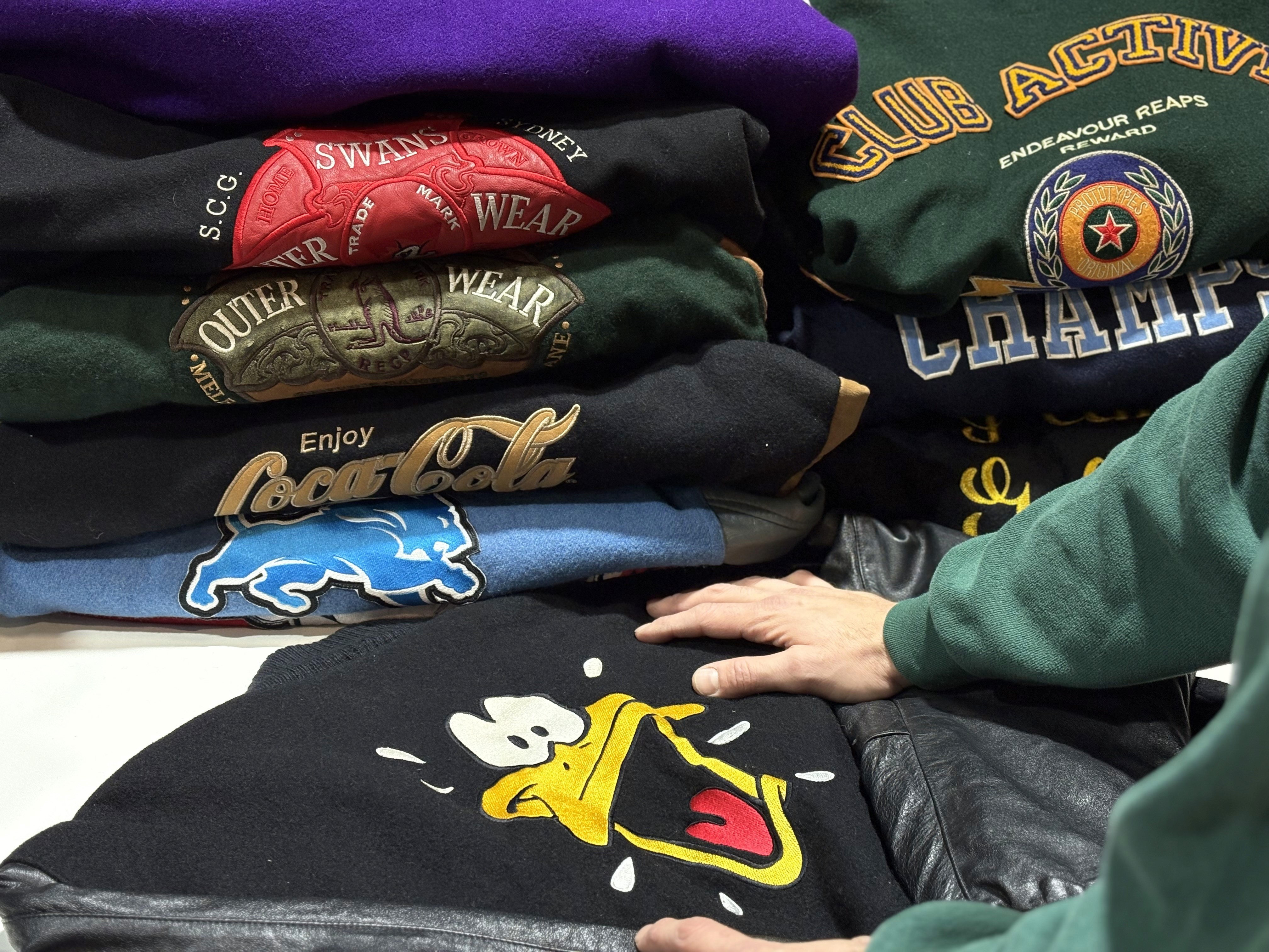 Pile of vintage sweatshirts with embroidered designs & leather jacket.