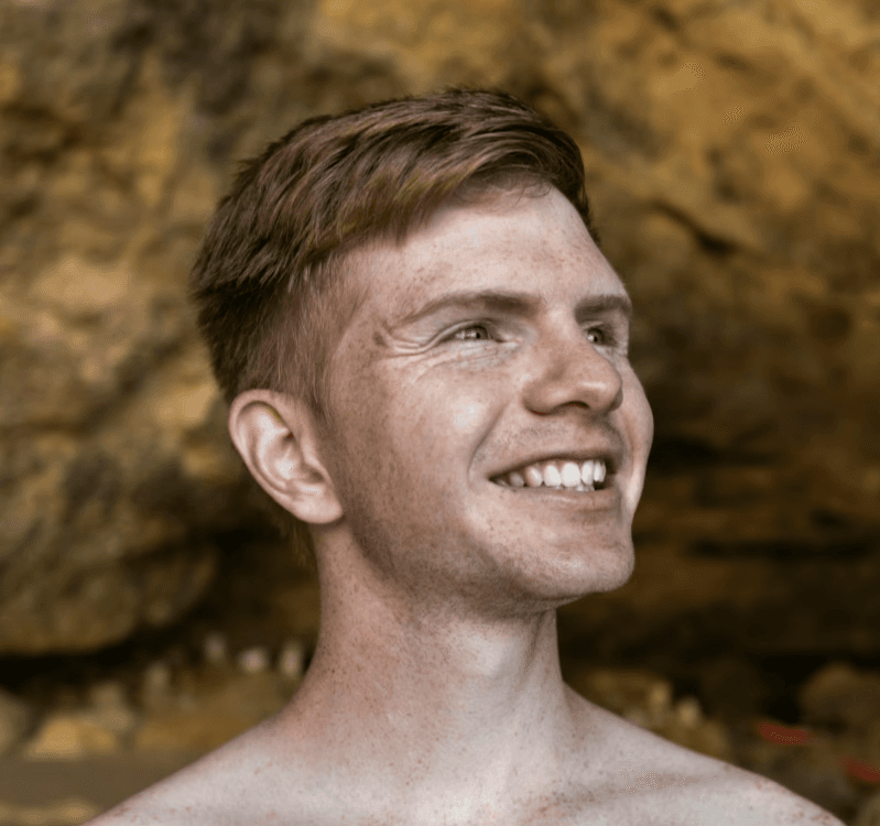 a young man wearing glasses standing in front of a mountain