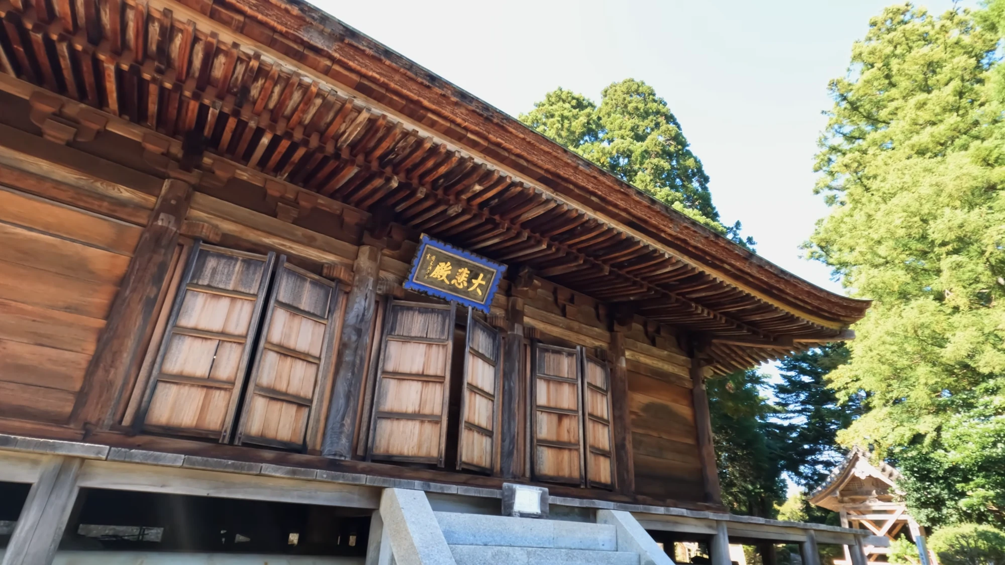 A timber temple hall at Onsenji above Kinosaki with autumn colour behind its roof.