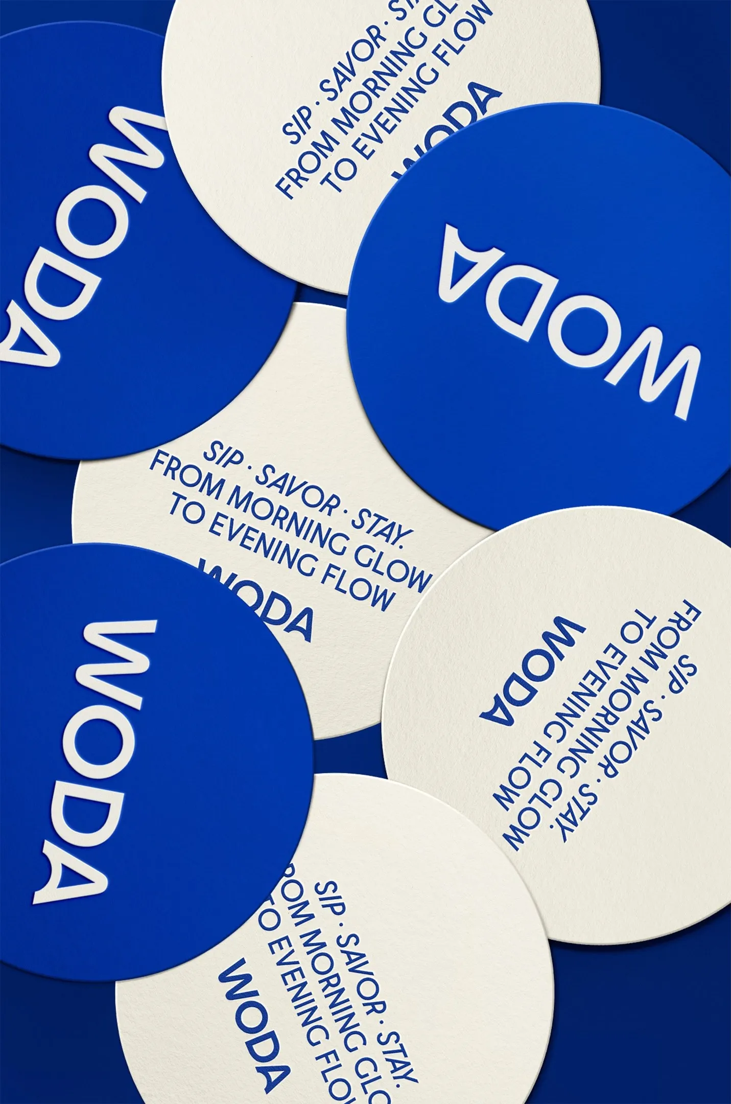 Scattered round Woda coasters in blue and cream with the tagline Sip, savor, stay, restaurant print collateral