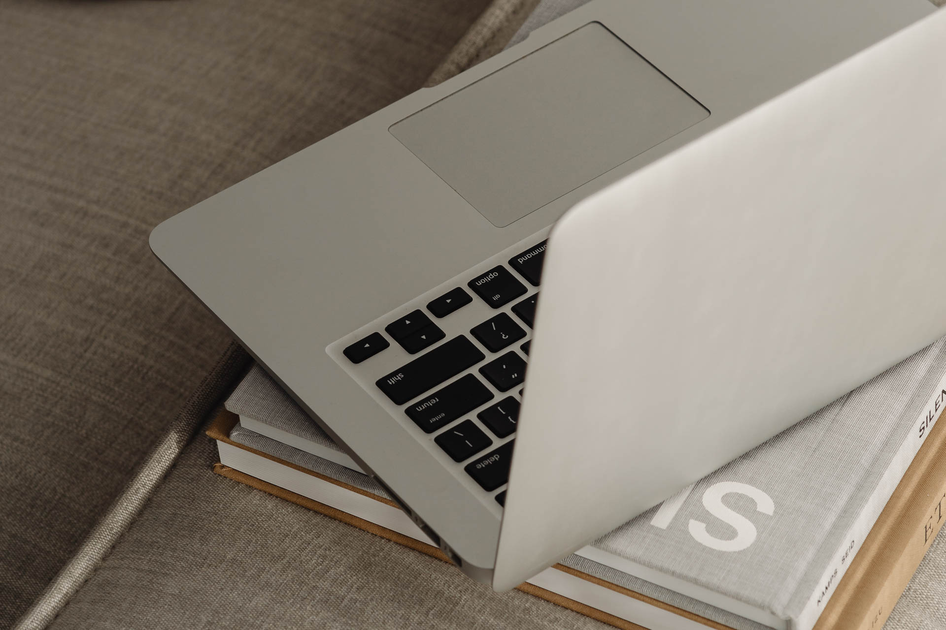 Silberner, geöffneter Laptop steht auf vielen Inspirations Magazinen, die auf einer Couch liegen