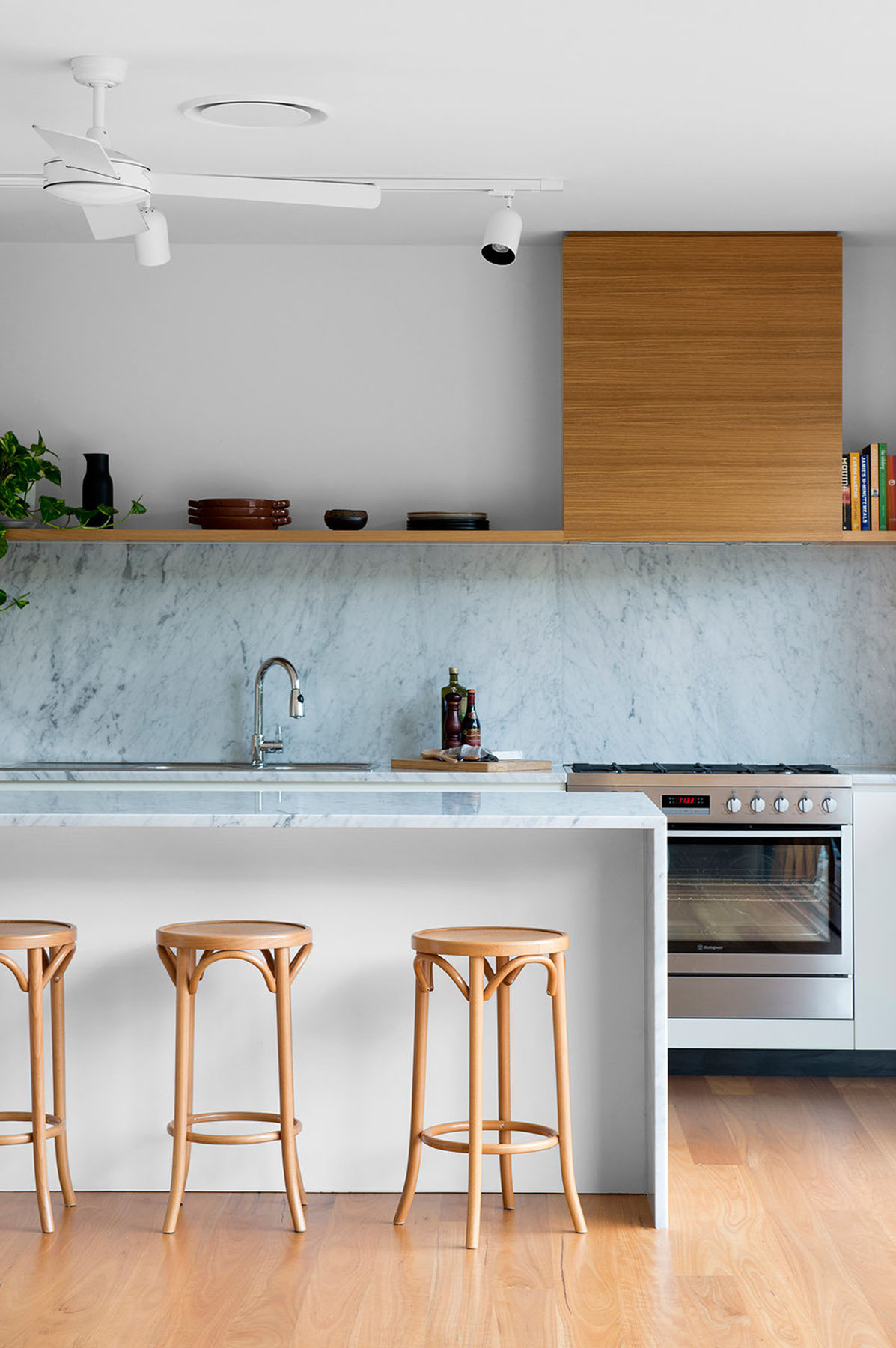Minimal kitchen with marble splashback, integrated joinery, and light timber accents under soft, even lighting.