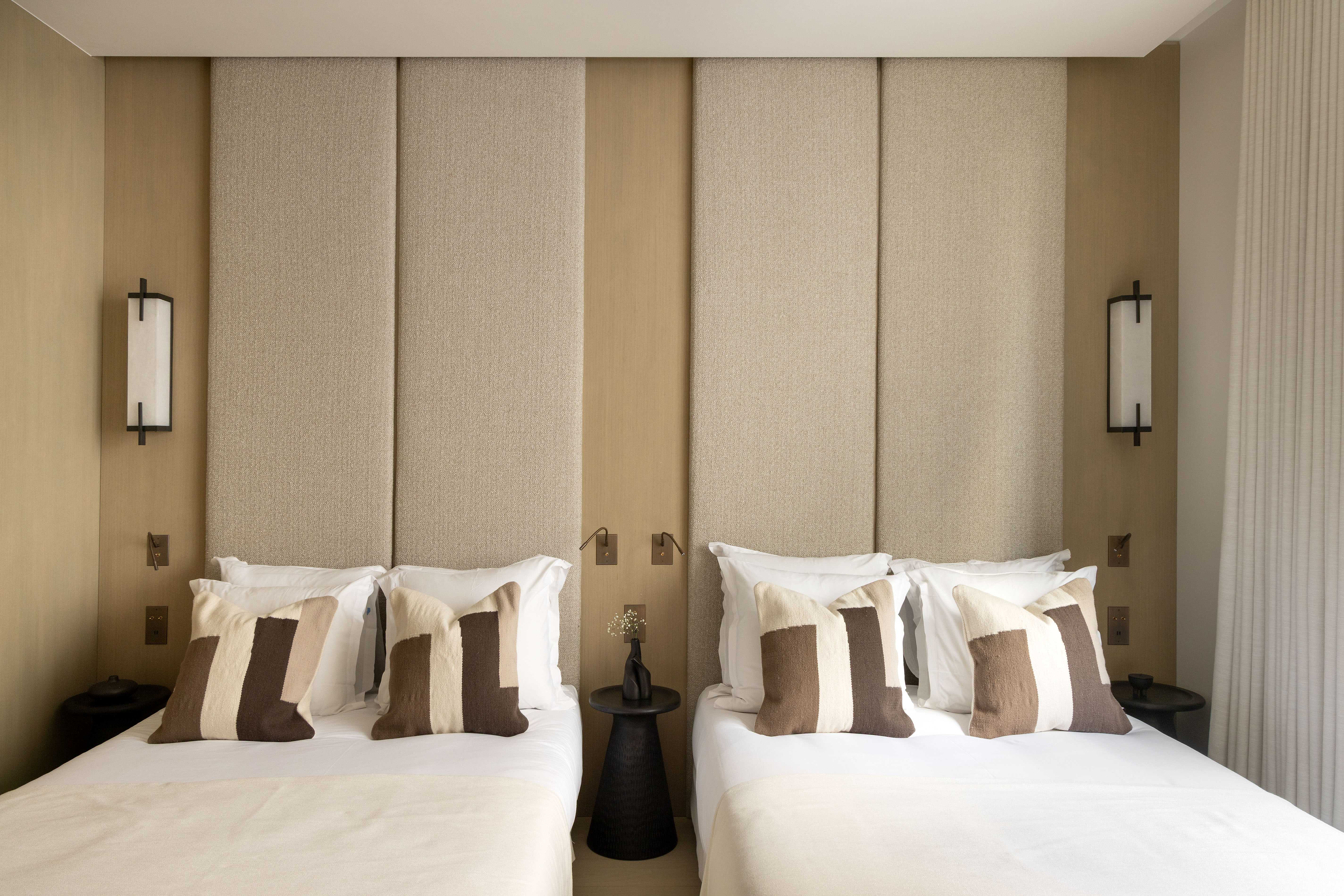 Chambre twin avec deux lits jumeaux, coussins bicolores beige et blanc, appliques murales