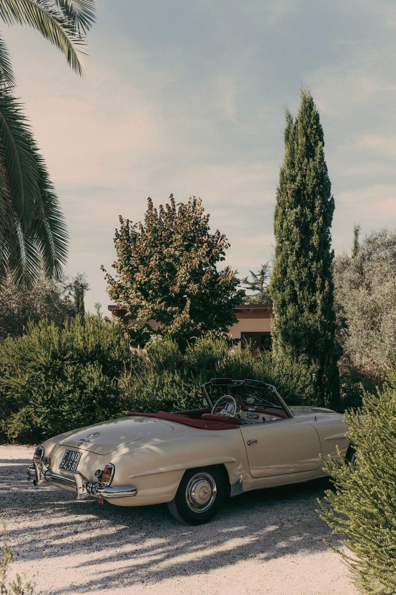 Porsche cabriolet bianca d'epoca nella campagna di Bolgheri tra cipressi e ulivi al tramonto