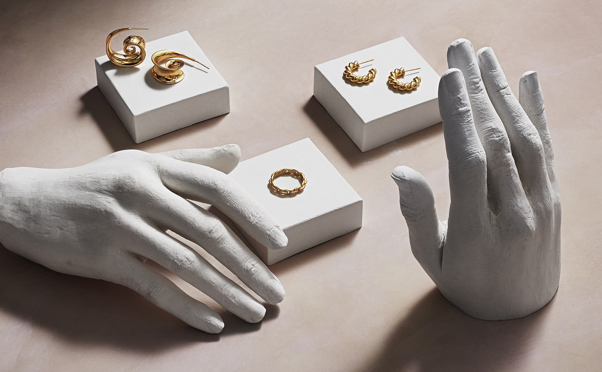 Gold jewelry earrings and ring on white display stands with sculpted hands.