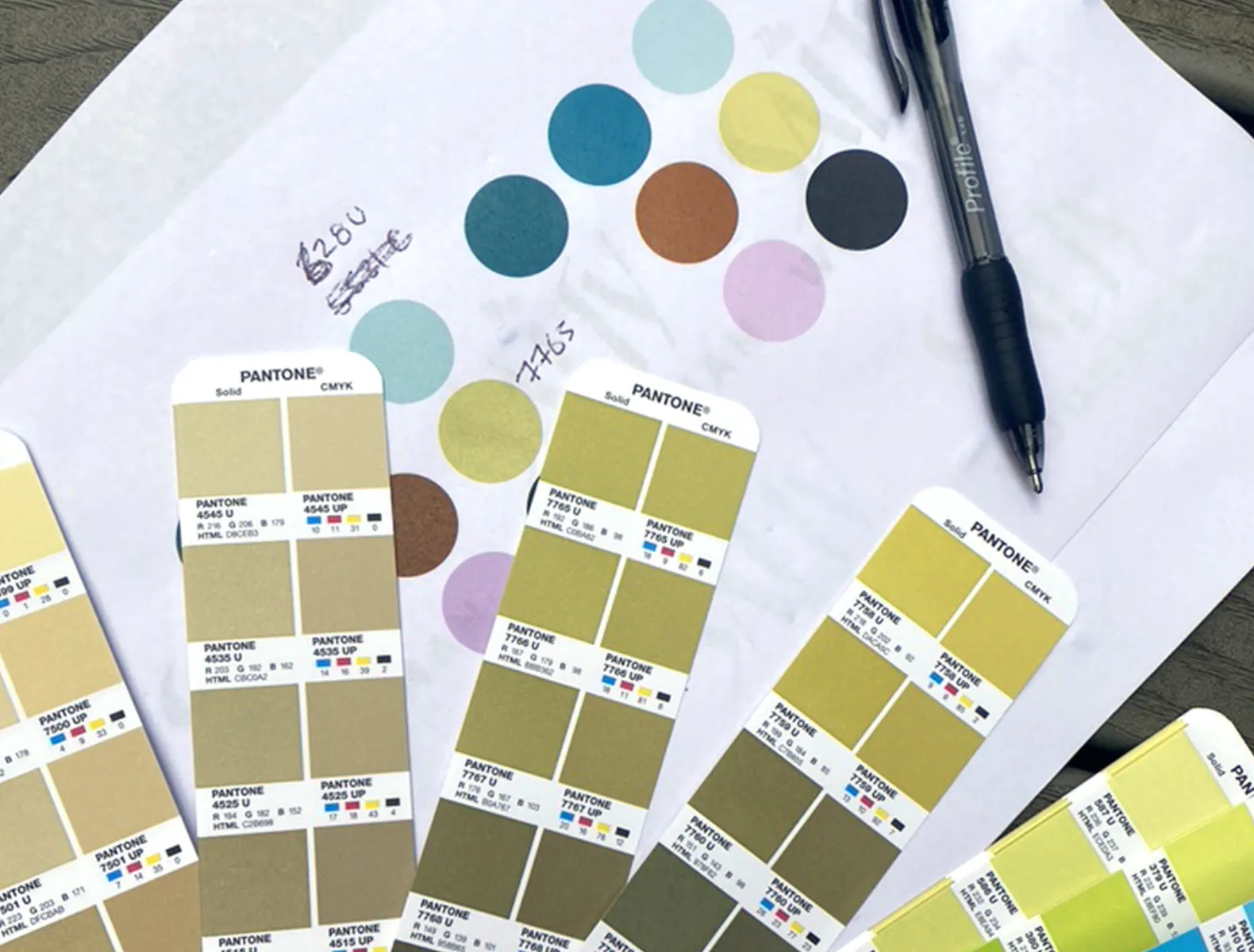 A printout of colour swatches with notes written in pen and a Pantone Colour Bridge book overlayed on top with various yellow swatches open.
