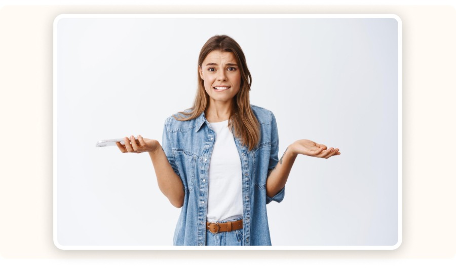 Femme perplexe hausse les épaules, téléphone en main, fond blanc.&nbsp;