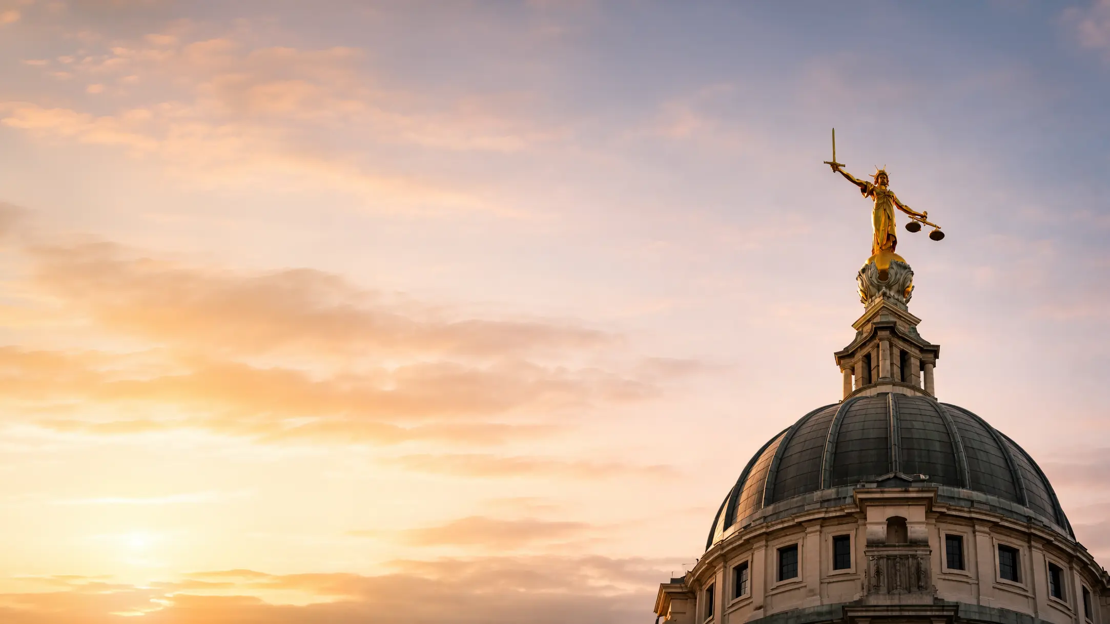 Lady Justice statue atop a dome at sunset.