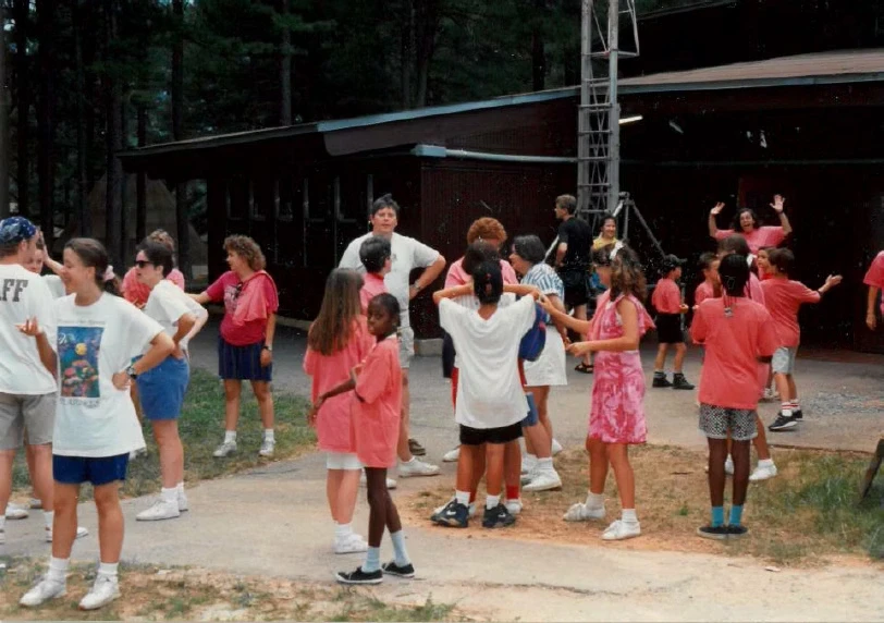 A large group of campers and staff are gathered outside a building at Camp Juliena. Many are wearing pink shirts.