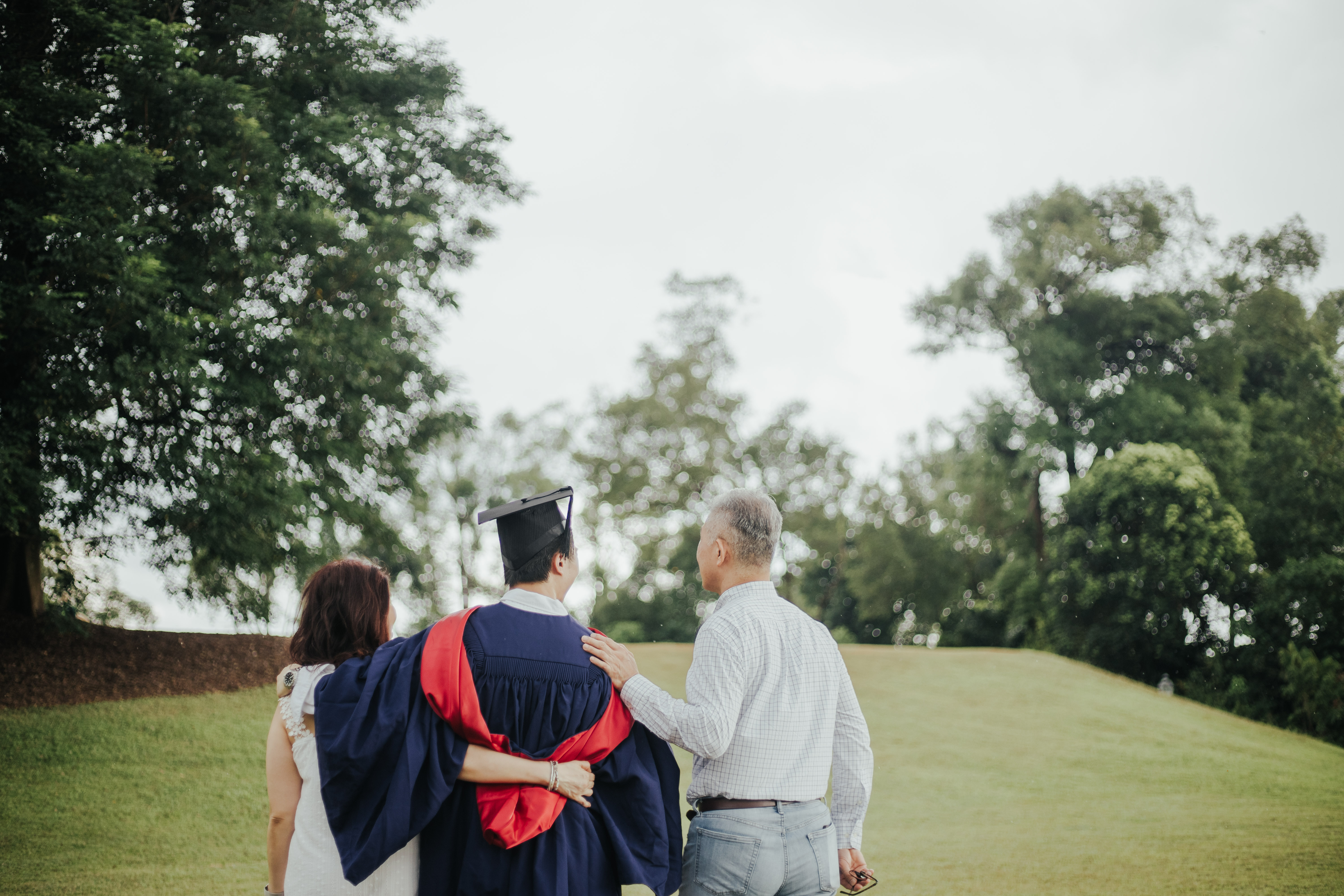 Family photo: Graduate posing with proud parents near the Bandstand at Botanic Gardens.
