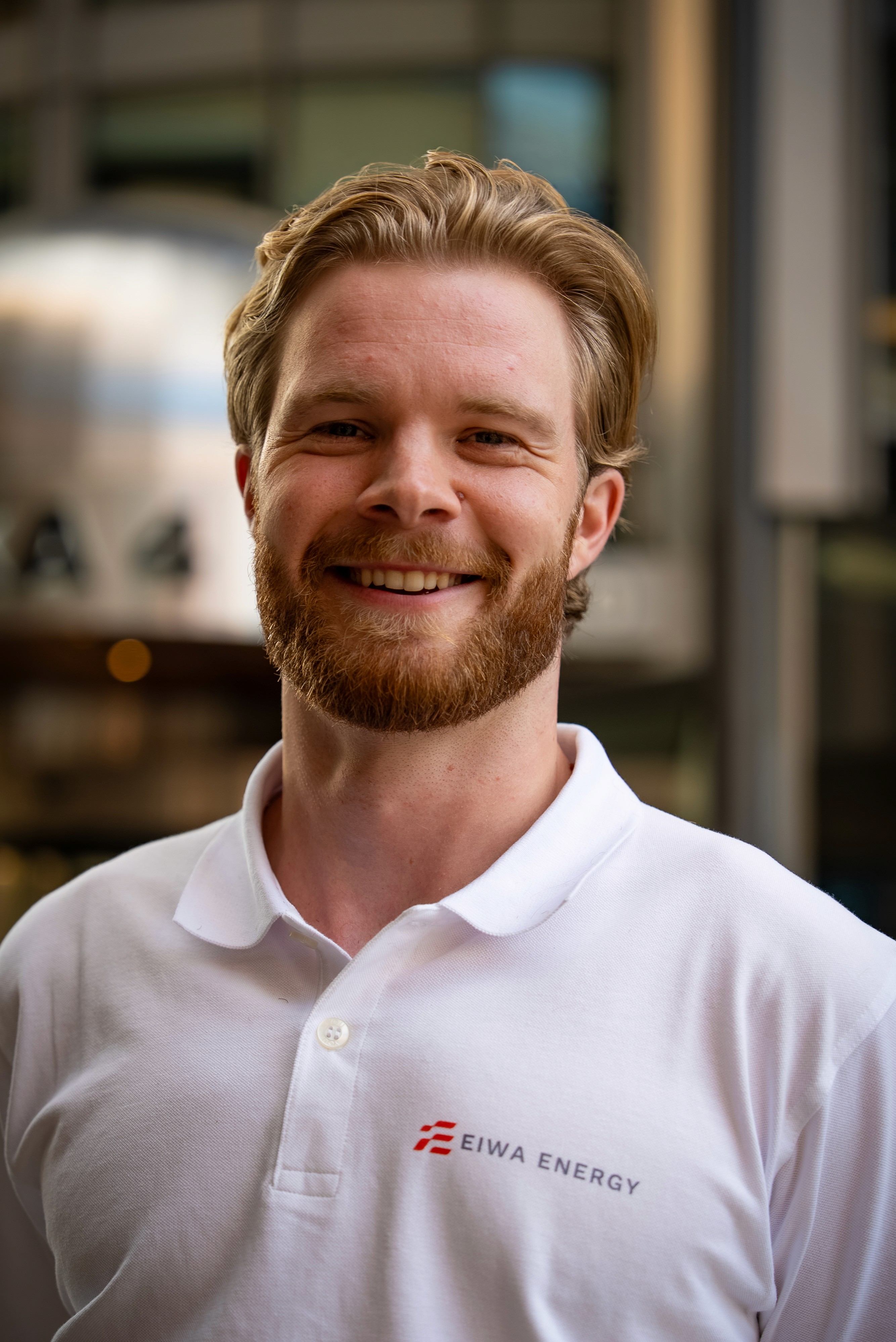 Smiling woman with curly hair and glasses using a smartphone in an office setting.