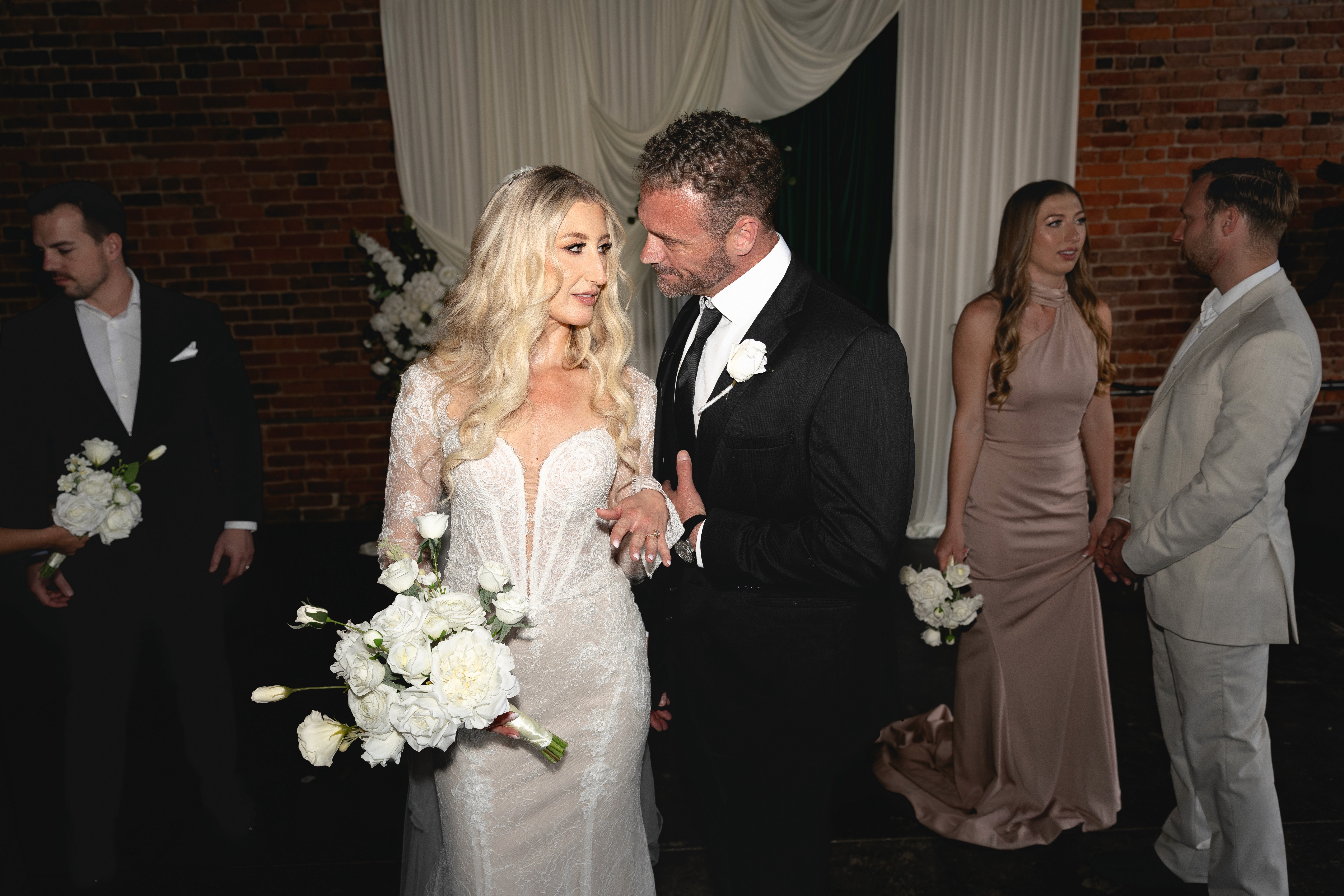 A couple embraces and smiles under a tall, green, steel bridge.