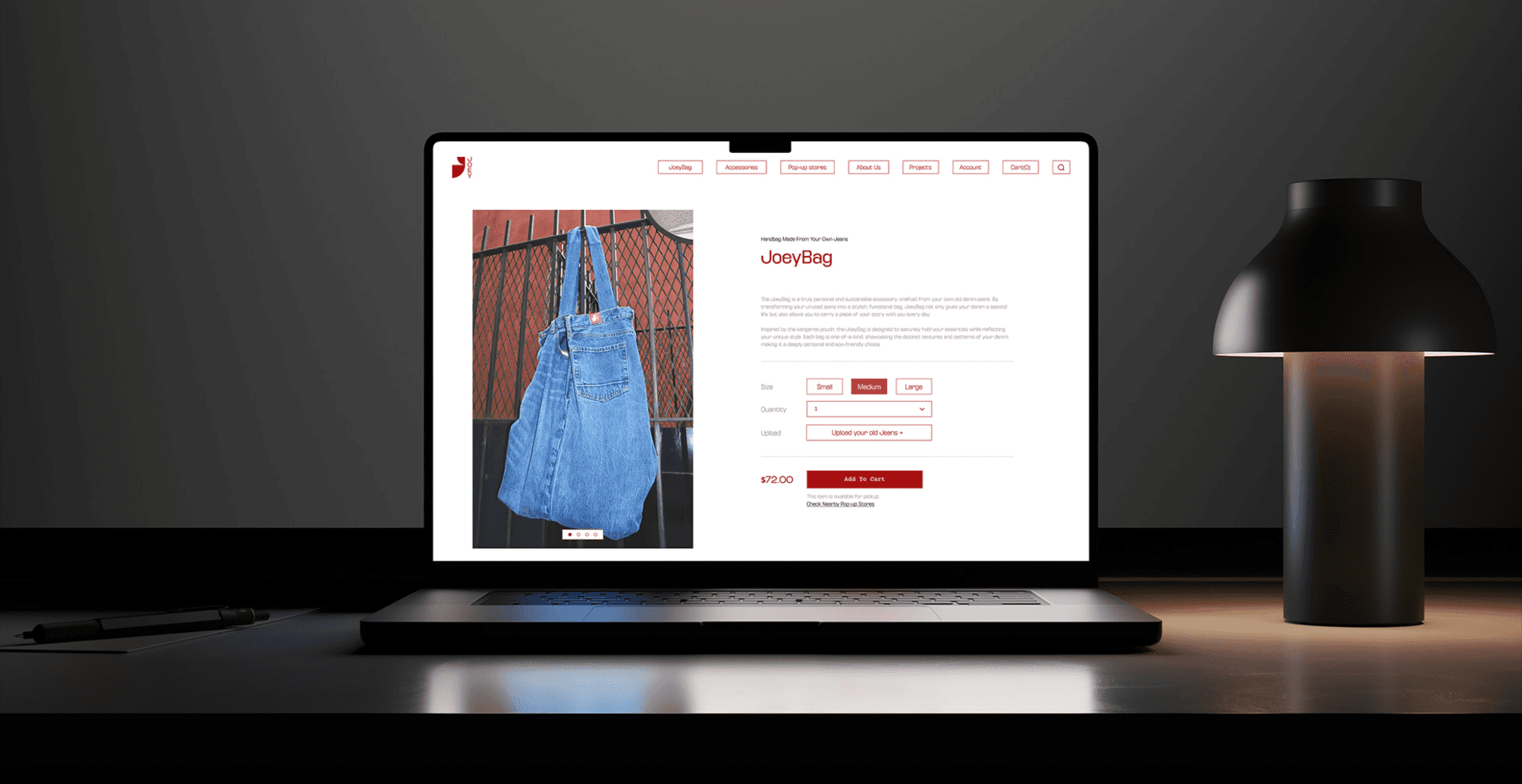 A laptop screen displays a product page for "JueyBag," featuring a blue denim bag hanging on a metal fence. The page includes product details such as "Size," "Quantity," "Quality," "Color," "Price," and "Shipping," along with options for adding to cart or checking out. A black lamp with a white shade sits to the right of the laptop, and a pen rests on a dark surface to the left. The background is dark and blurred.