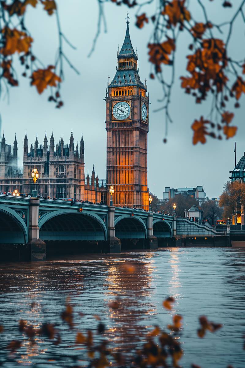 A view of Big Ben and the Houses of Parliament illuminated at dusk, framed by autumn leaves. The Thames reflects the scene's warm glow, creating a serene atmosphere.