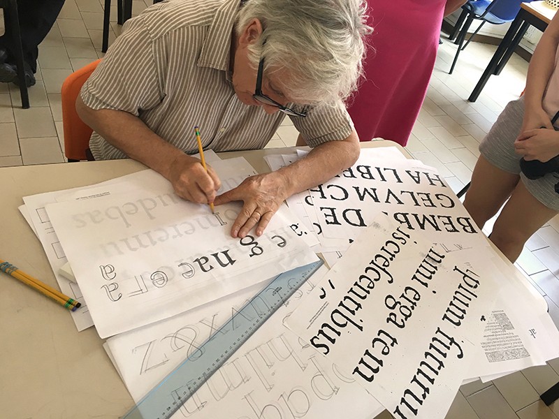 A man with glasses copying letters at a desk.