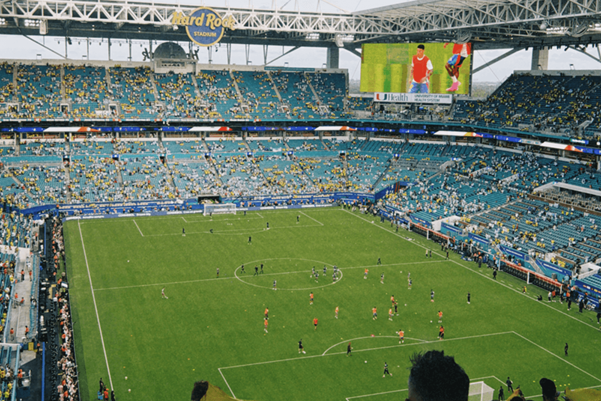 Packed football stadium with a match in progress under bright floodlights