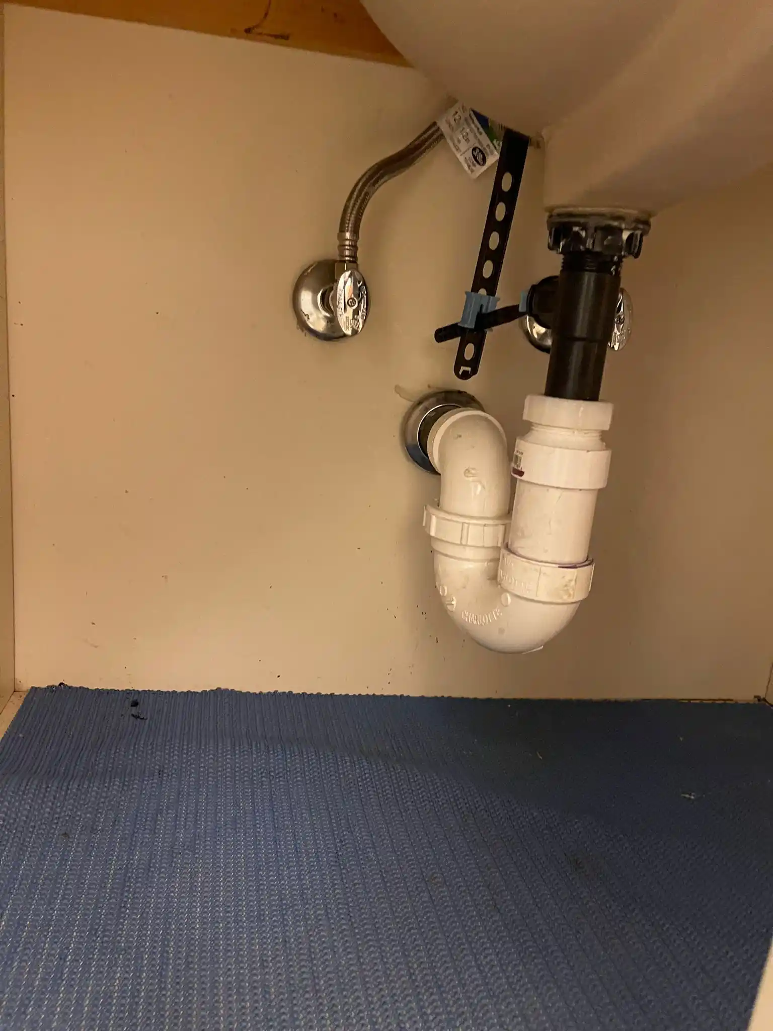A clean under-sink cabinet showing a newly connected PVC P-trap, drain assembly, and shutoff valve completed during a bathroom sink repair.