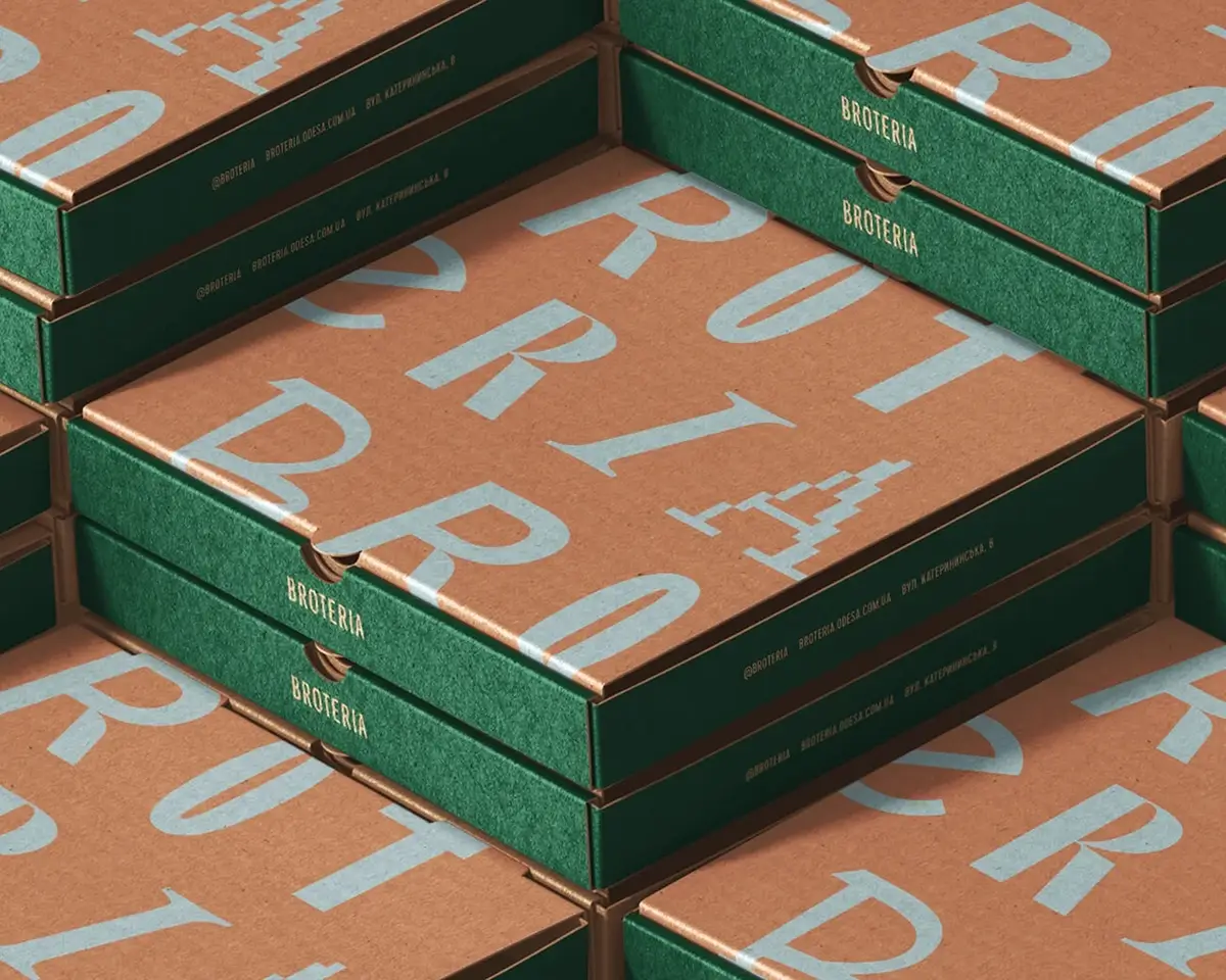 Stack of green and kraft Broteria bakery boxes with large blue letter graphics
