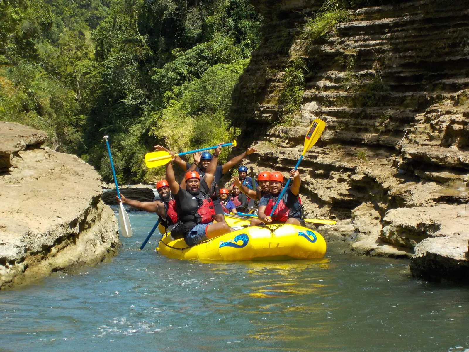 Upper Navua River Rafting People in a yellow raft enjoy Pacific Harbour activities, cheering and paddling between jungle and rock walls.