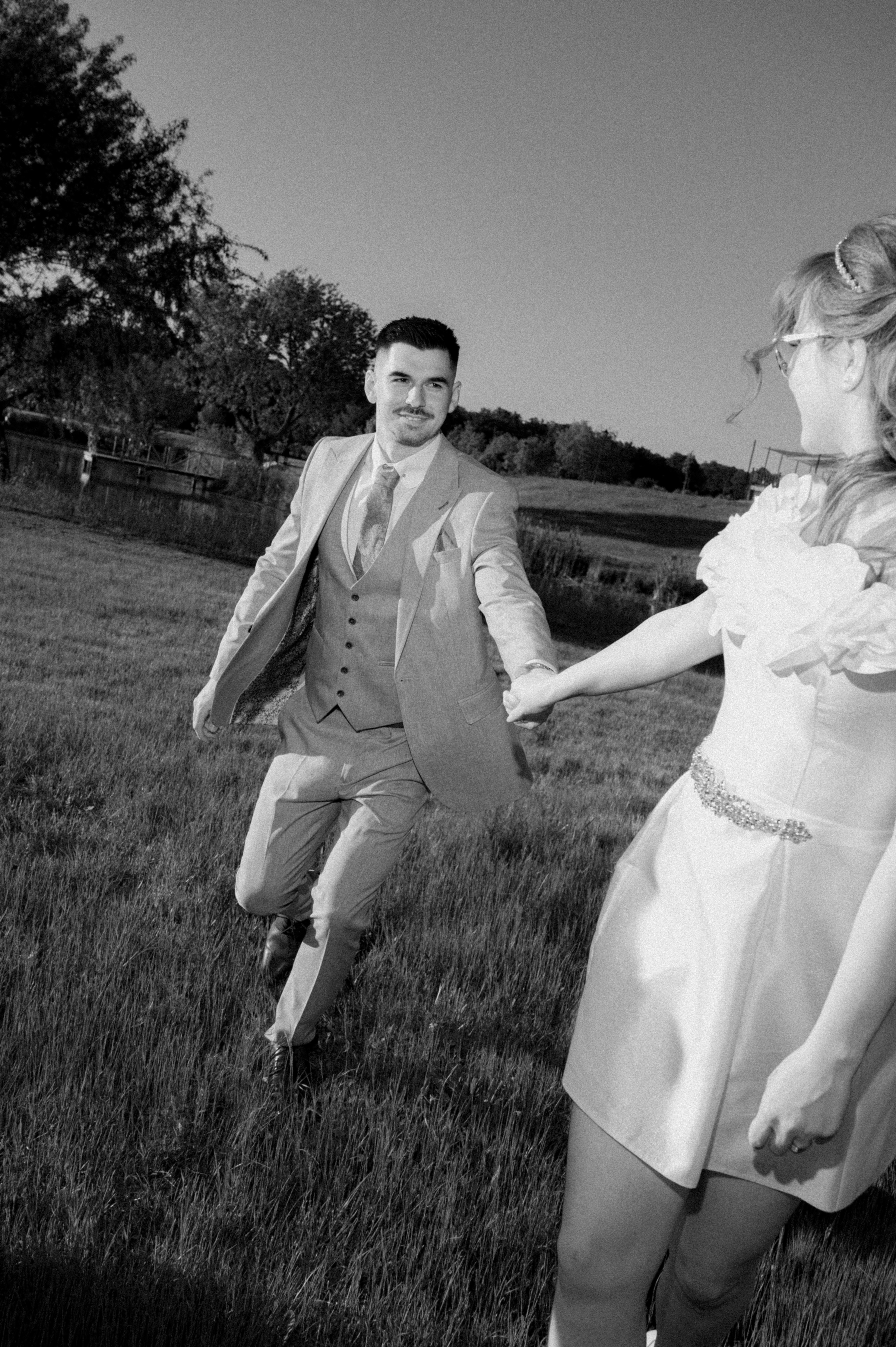 Mirii ținându-se de mână după ceremonia civilă pe malul lacului, fotografie documentară cu lumină naturală.