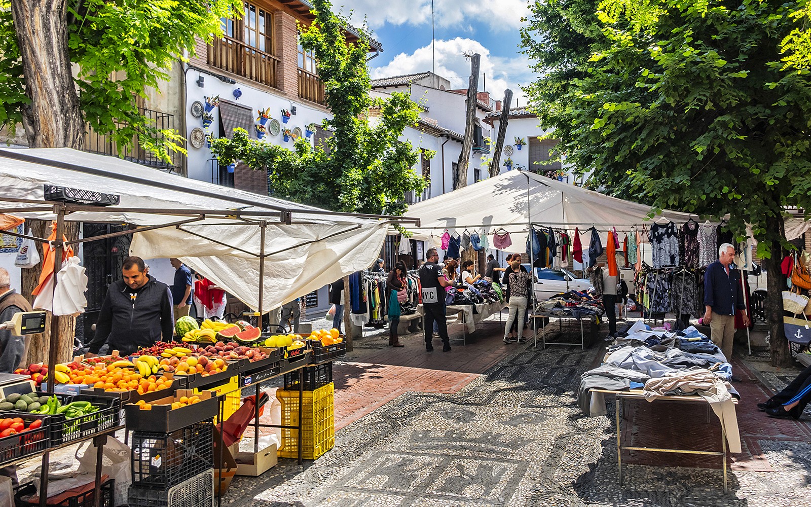 Outdoor market in Albaicin, Granada with stalls selling fruits, clothes, and local crafts.