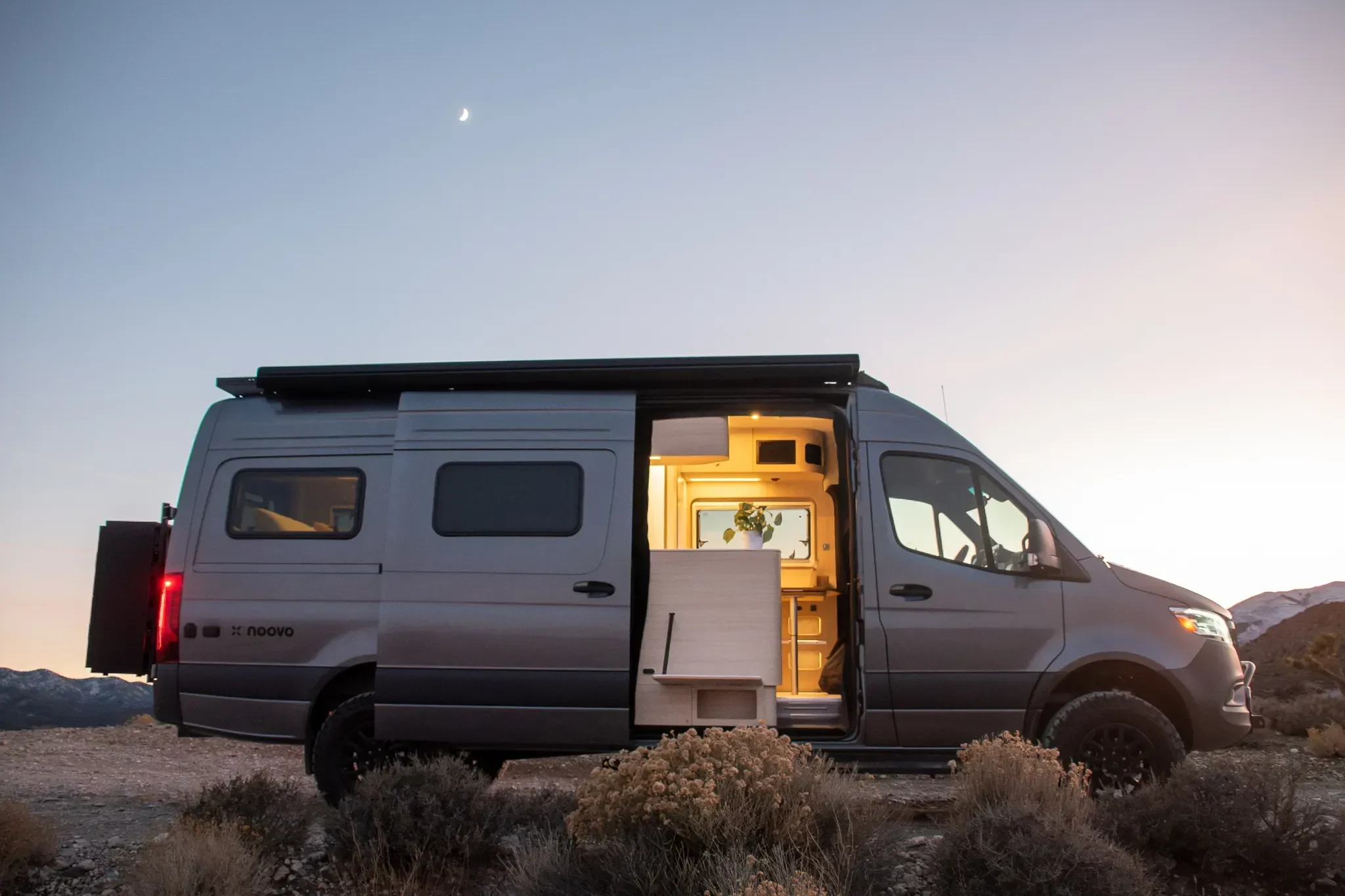 Camper van parked in the desert at dusk, interior lights glowing