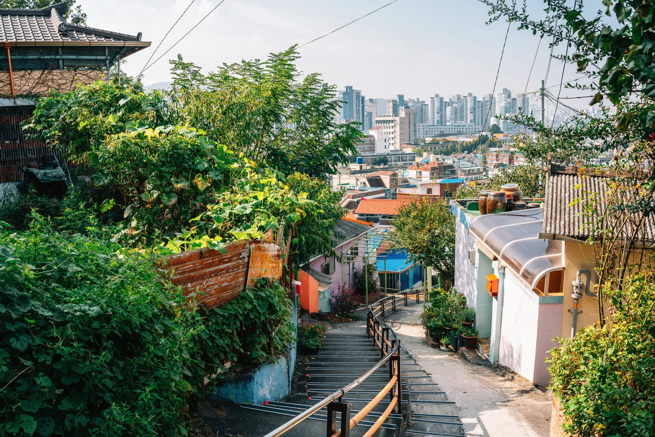 a view of an old neighborhood in seoul with narrow stairs leading down a slope. in the background, modern high rises are visible