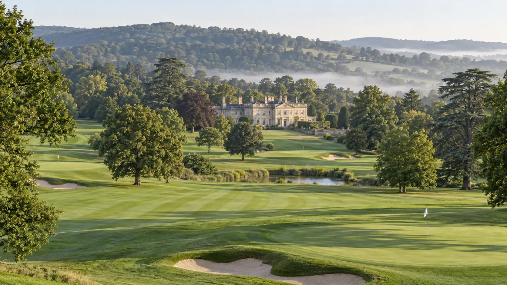 The course from the hill above the eleventh: striped fairways between oaks and cedars, the mere, and the House in the middle distance