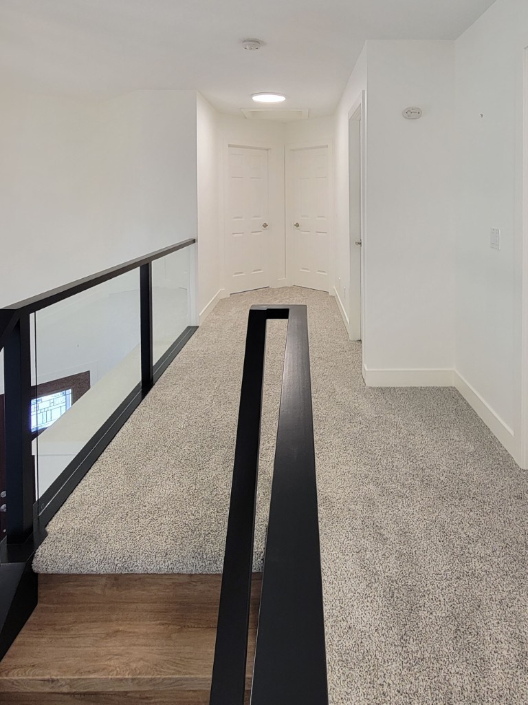 Image of KHD Homes interior design featuring carpeted hallway with modern railing and wood staircase leading to rooms.