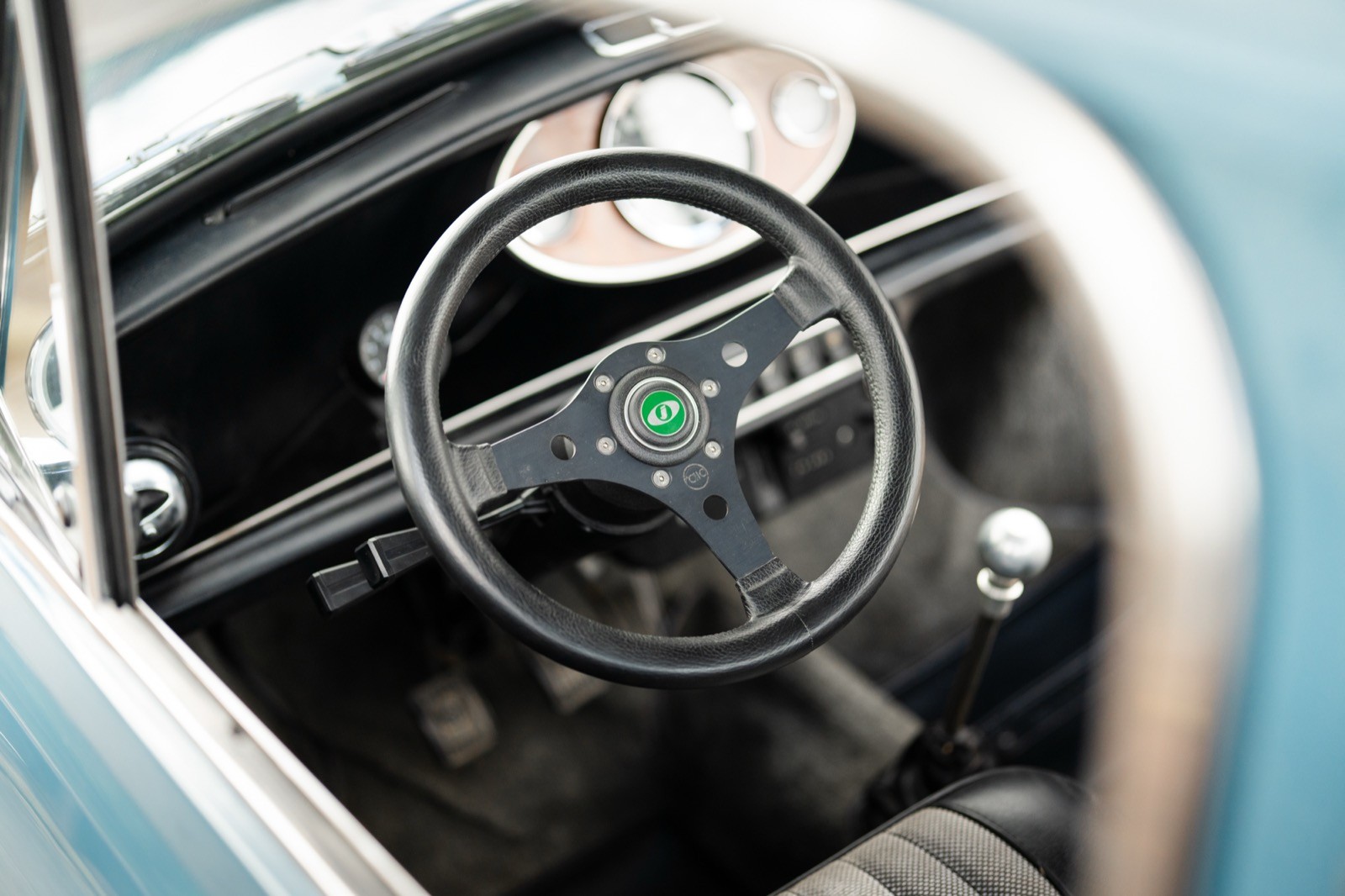 Close-up view of an old car's dashboard, featuring a steering wheel, speedometer, and vintage controls.